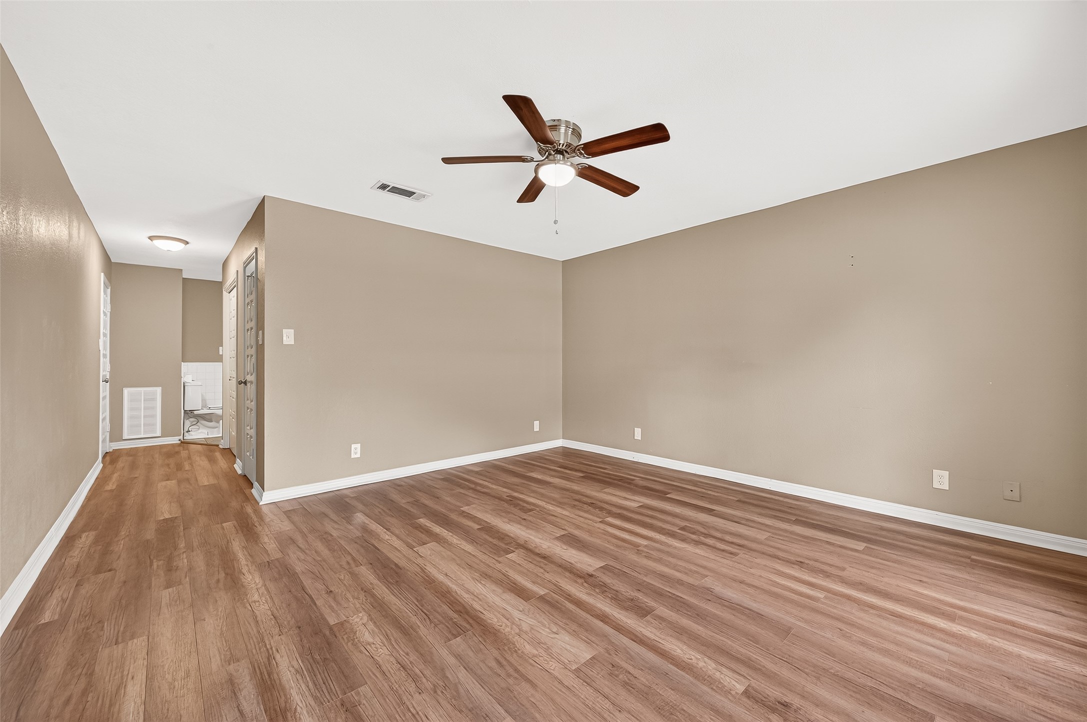 This primary bedroom features warm wood flooring, neutral walls, and a ceiling fan, creating a comfortable and inviting atmosphere. The open layout offers versatility for various furniture arrangements.