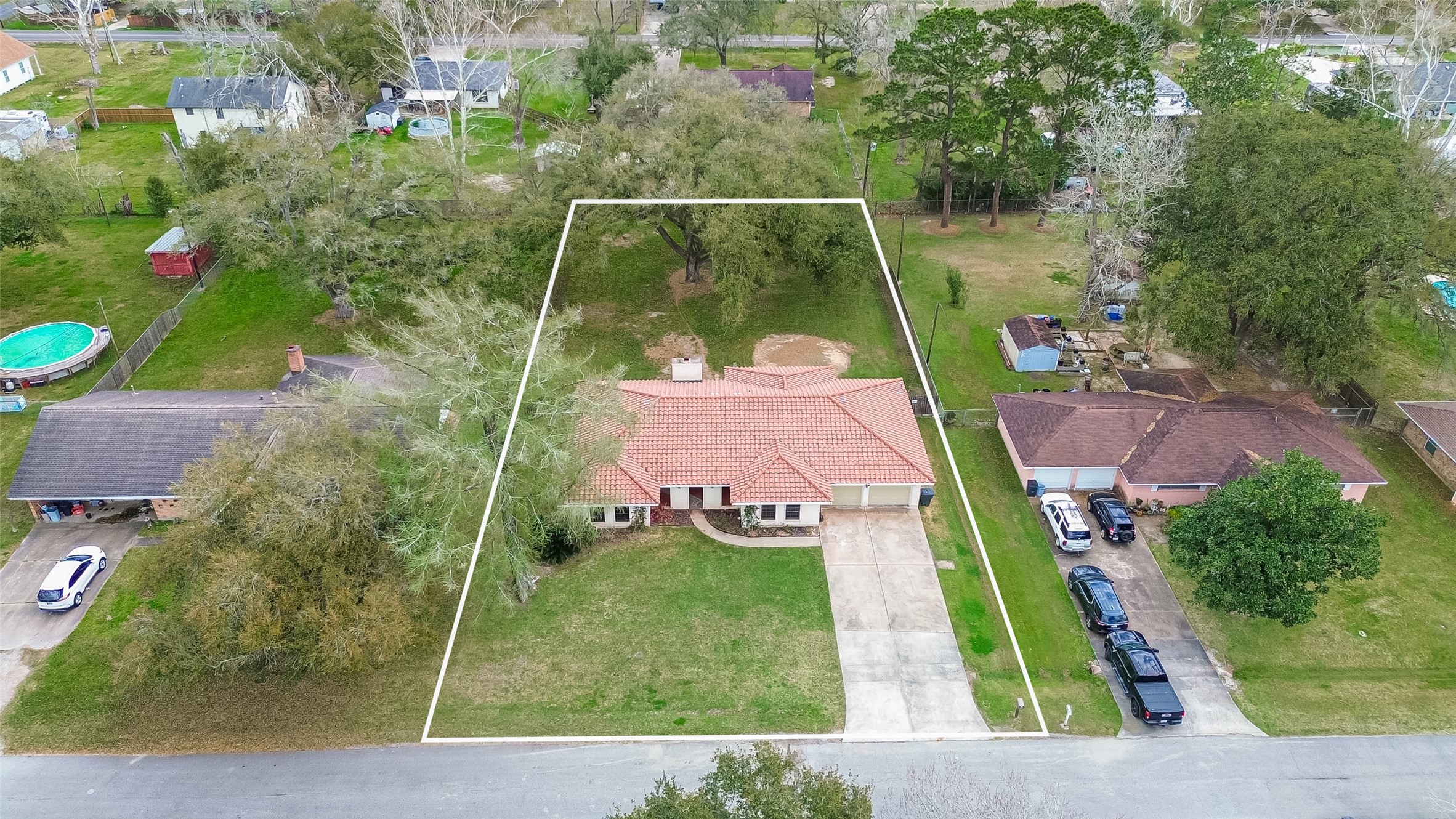 This property features a charming single-story home with a red-tiled roof and a spacious front yard. It includes a long driveway leading to a two-car garage. The large backyard is surrounded by mature trees, offering privacy and a natural setting. Located in a quiet neighborhood, it provides ample outdoor space for relaxation and activities. Photo shows outline of property.