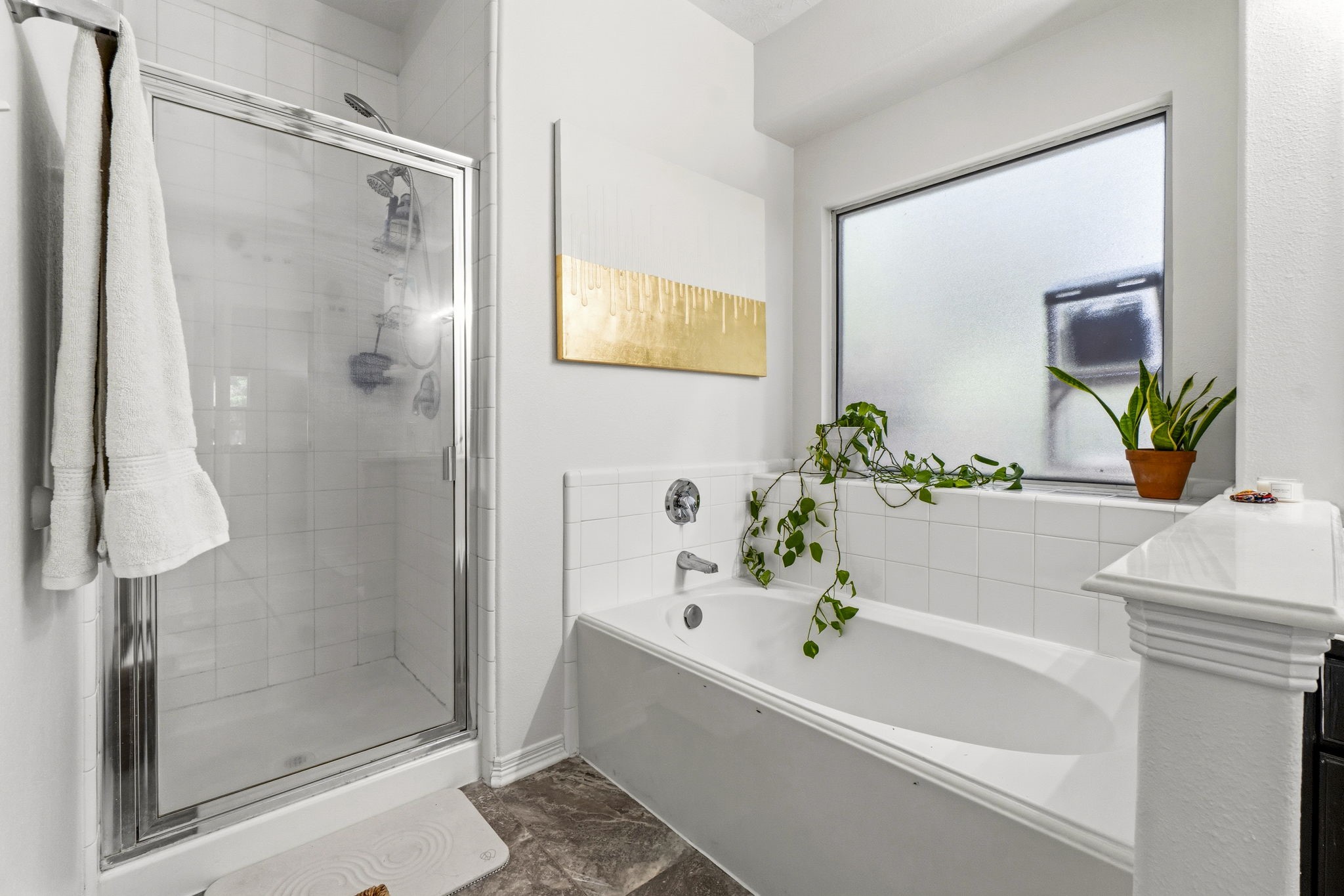 Bright, modern bathroom featuring a sleek glass shower, spacious bathtub, and ample natural light from a frosted window, complemented by elegant tile work and greenery.