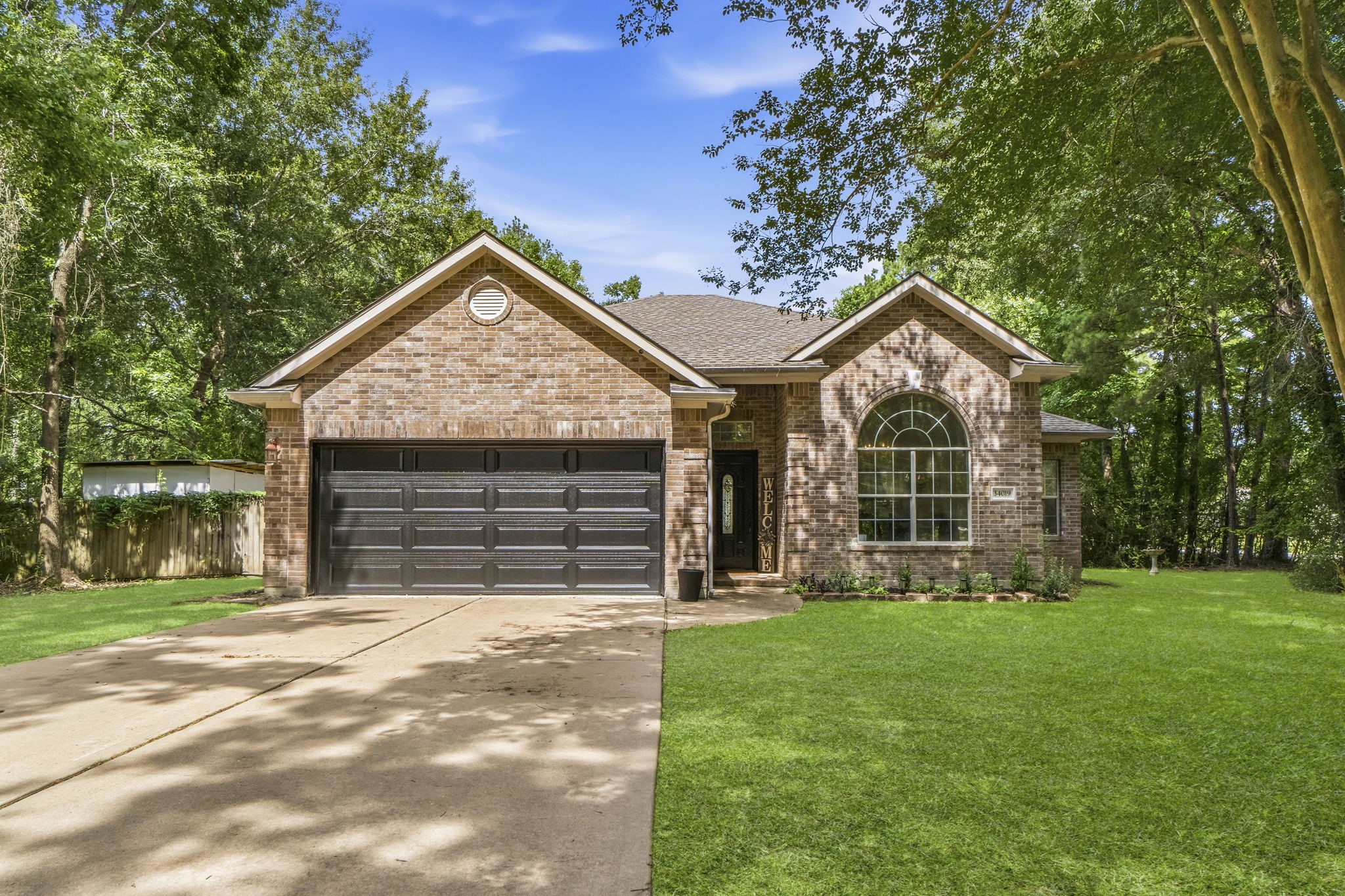 Charming brick home with a spacious two-car garage, nestled amidst lush greenery and mature trees, offering a serene and inviting curb appeal.