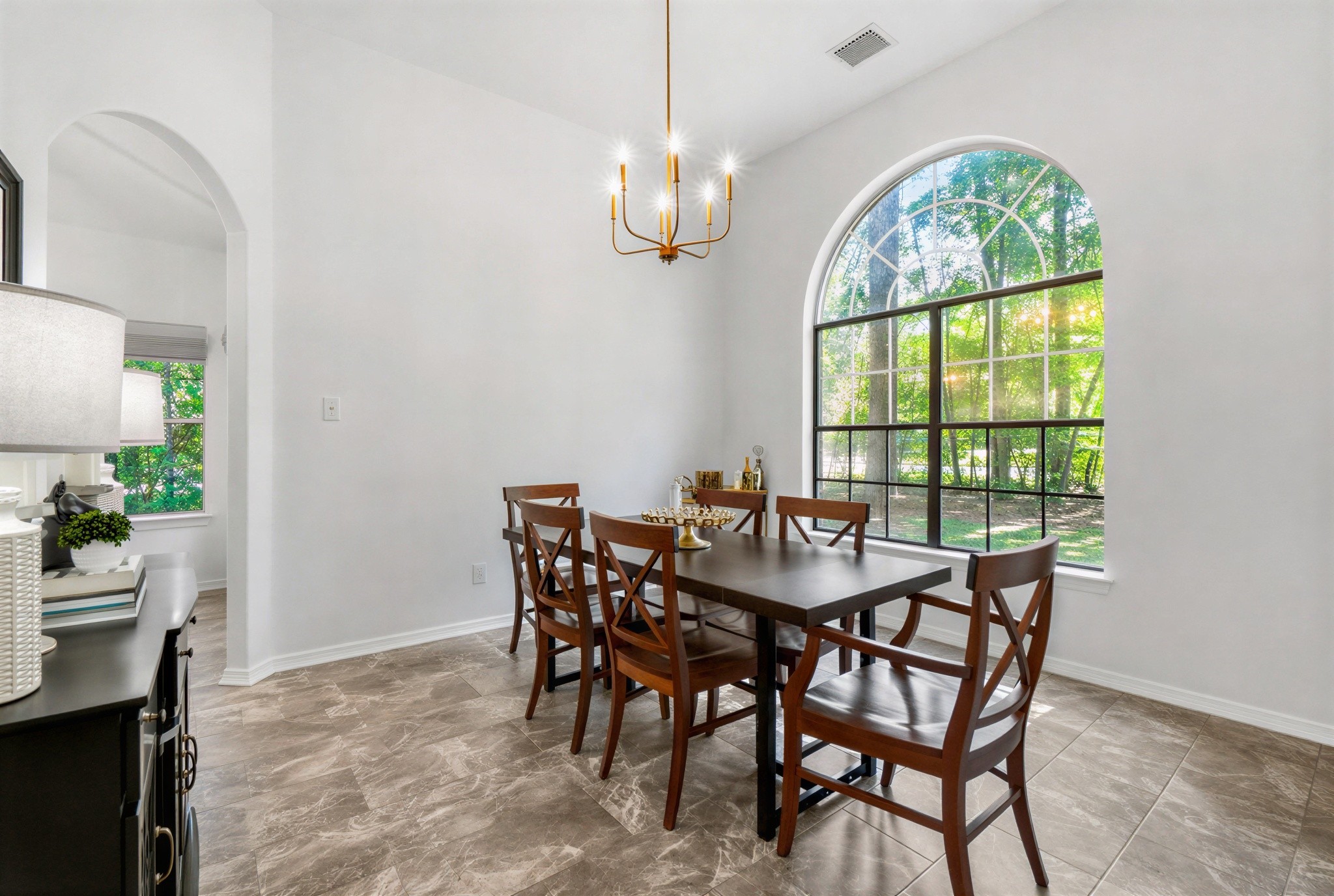 Bright dining area with a large arched window, elegant chandelier, and stylish tile flooring, perfect for entertaining.