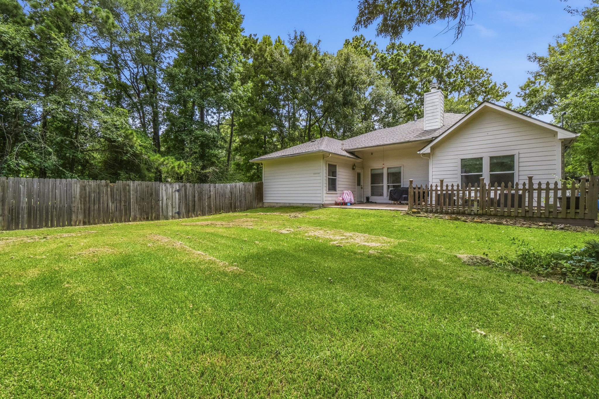 Charming single-story home with a spacious, fenced backyard surrounded by lush trees, offering privacy and a serene outdoor retreat.