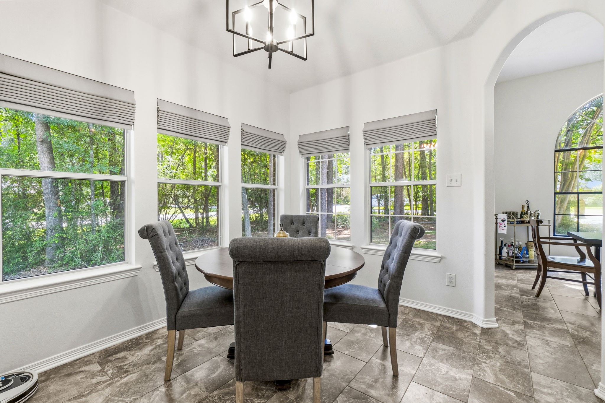 Bright dining area with large windows offering serene views of lush greenery, complemented by stylish tile flooring and modern lighting.