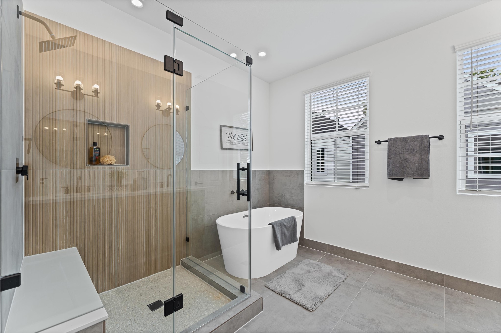 This luxurious primary bathroom blends modern elegance with spa-like comfort, featuring a spacious layout and contemporary selections throughout. A sleek double vanity with minimalist cabinetry and quartz countertops offers ample storage and style, while the glass-enclosed shower includes a built-in bench for added relaxation and convenience. The centerpiece is a sculptural freestanding soaking tub, perfectly positioned to invite unwinding after a long day.