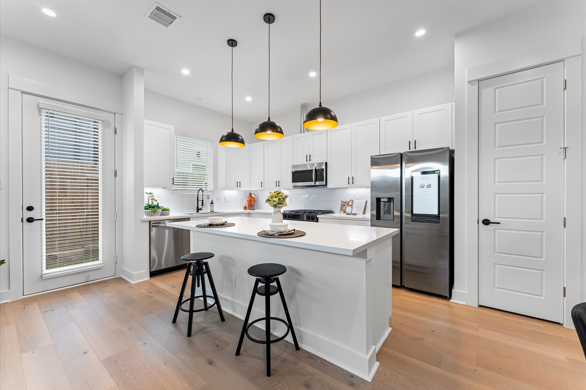 This centrally positioned kitchen island serves as a stylish anchor within the open-concept layout, offering clear sightlines to the dining area, living space, and the backyard beyond. Its placement encourages seamless interaction, whether prepping meals or entertaining guests, while natural light pours in through the nearby windows. The islands sleek design and functional surface make it a hub of activity, framed by elegant finishes tying together comfort and sophistication.