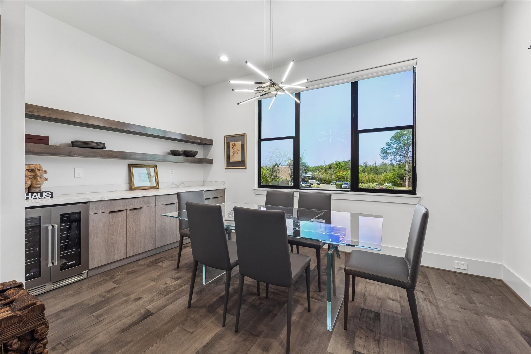 The elegant dining room features a modern chandelier, large window with sunset views, sleek cabinetry, and a built-in wine cooler.