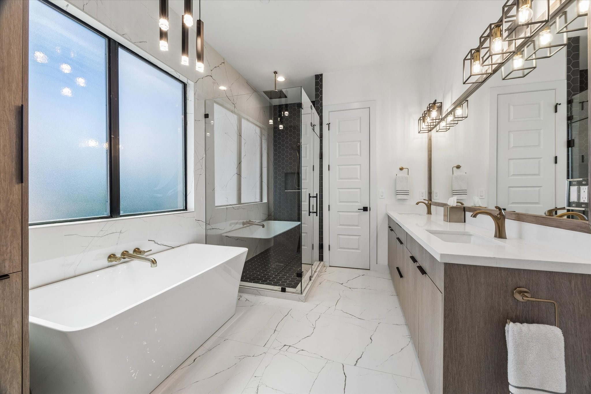Luxurious primary bathroom featuring a sleek glass shower, elegant soaking tub, dual sinks, and modern lighting for a spa-like retreat.