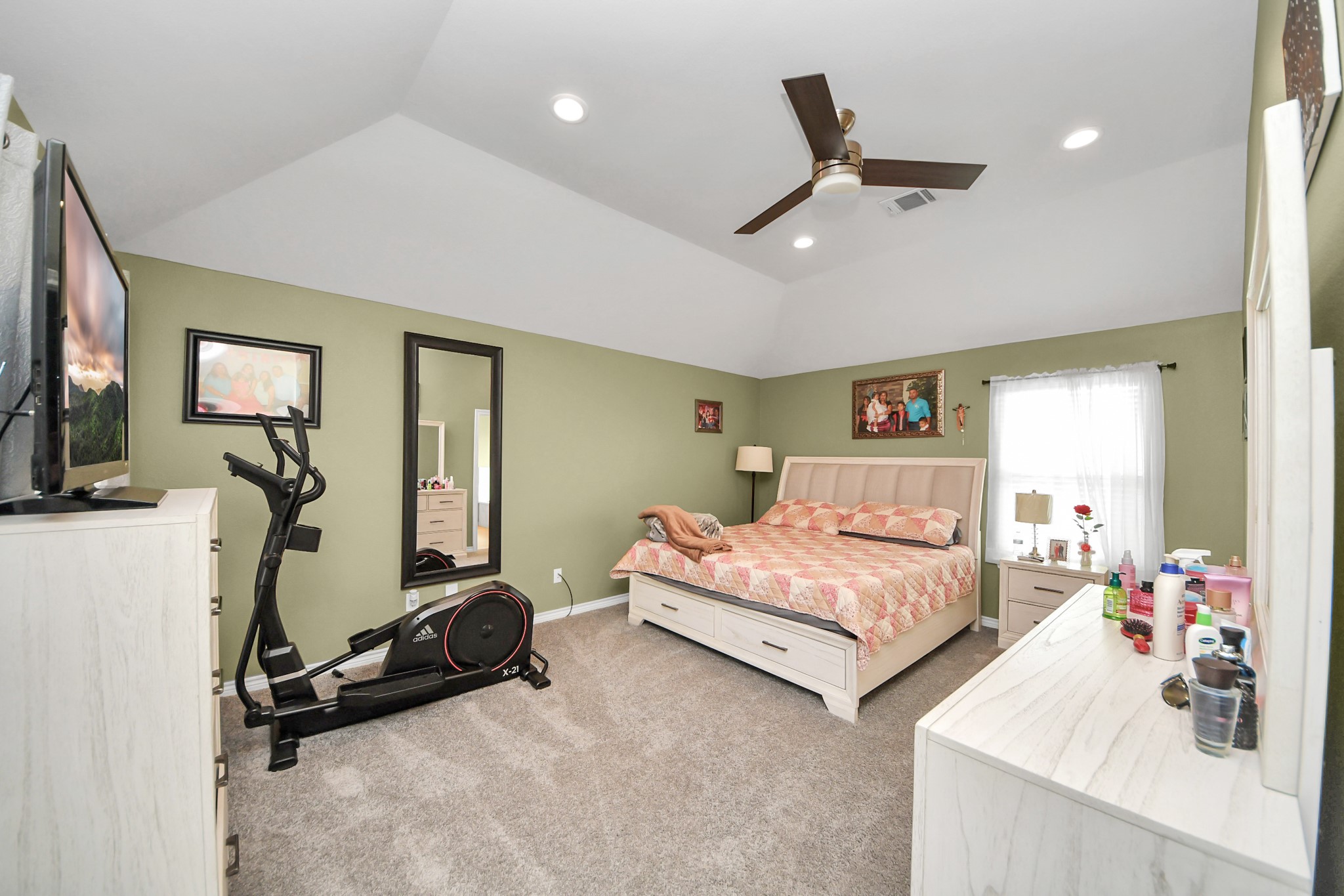 Primary bedroom with a tray ceiling, ceiling fan, and natural light.