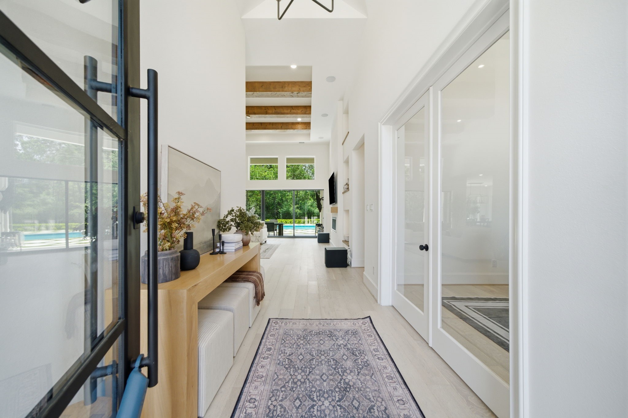 Elegant entryway with high ceilings, exposed beams, and abundant natural light leading to a view of the garden and pool area. Elegant entryway with high ceilings, exposed beams, and abundant natural light leading to a view of the garden and pool area.