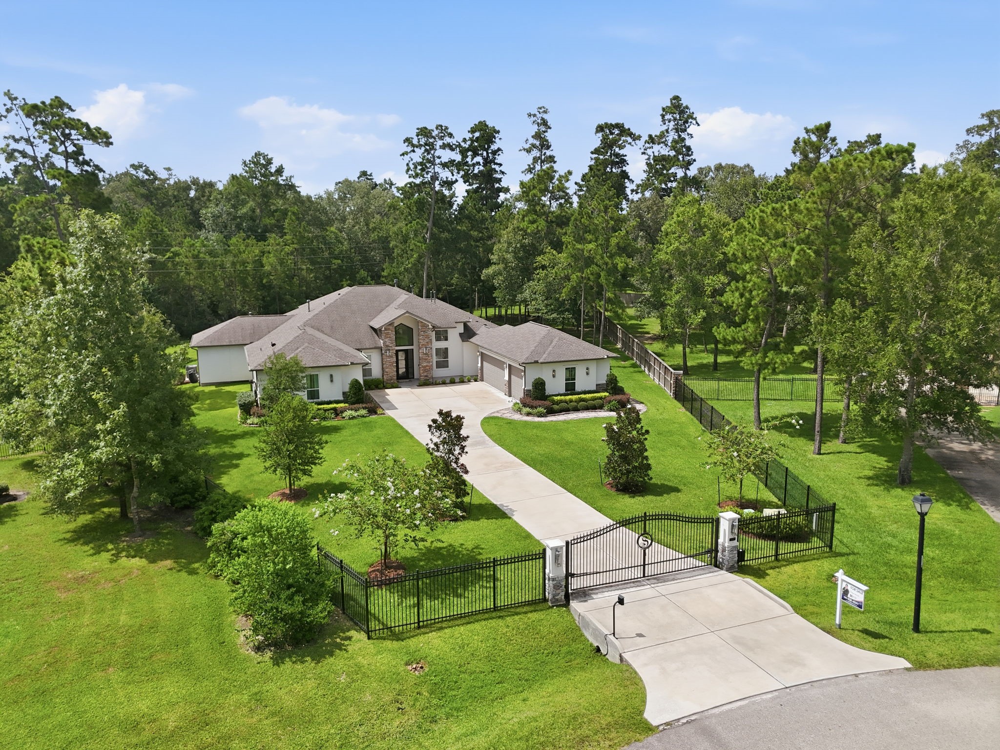 Stunning gated estate on a spacious, lush green lot with a long driveway leading to a charming single-story home surrounded by mature trees for ultimate privacy.