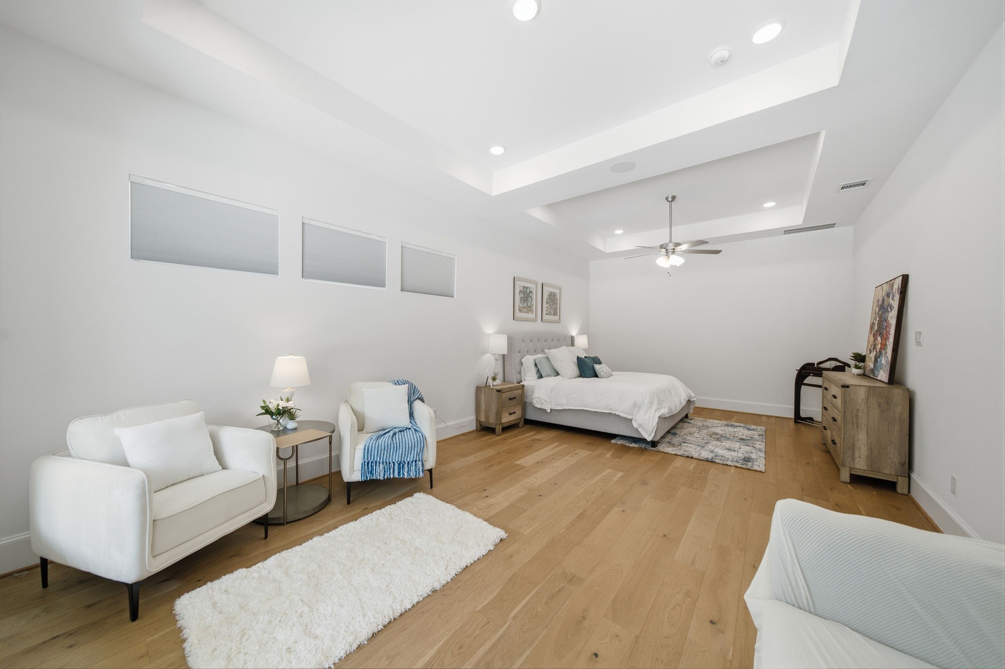 Spacious and elegant bedroom with hardwood floors, recessed lighting, and a cozy sitting area, offering a serene retreat.