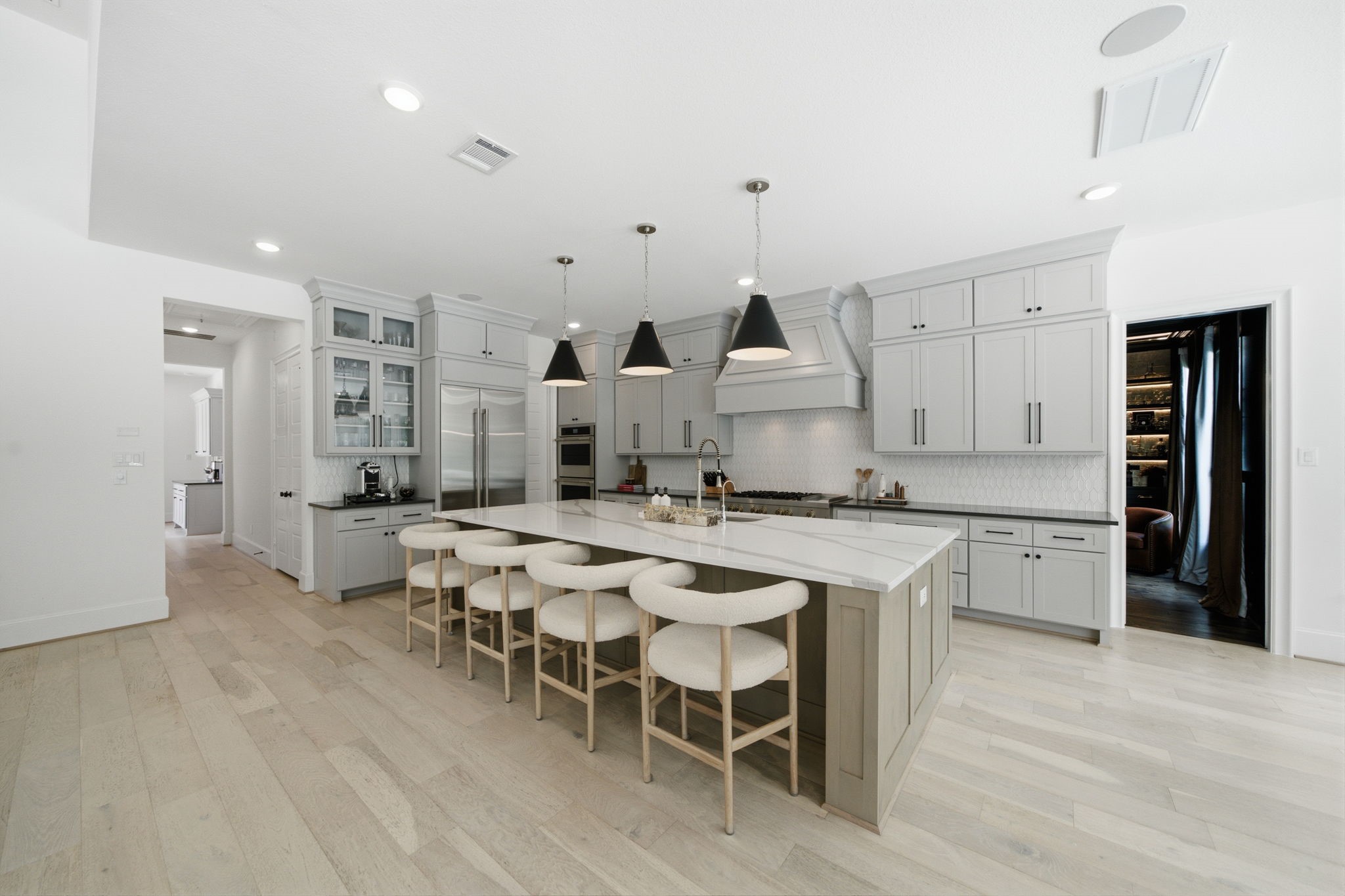 Spacious modern kitchen with sleek gray cabinetry, a large central island featuring elegant pendant lighting, and high-end stainless steel appliances.
