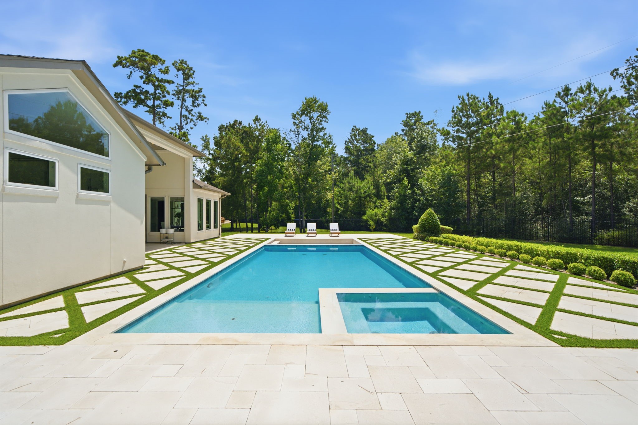 Luxurious modern home featuring a stunning outdoor pool and spa, surrounded by a beautifully landscaped yard with lush greenery and ample space for relaxation.