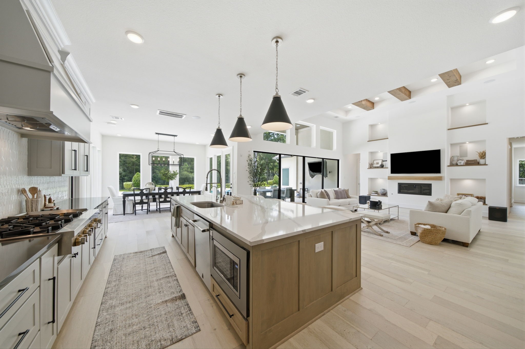 Spacious open-concept living area featuring a modern kitchen with a large island, elegant pendant lighting, and sleek cabinetry, seamlessly flowing into a bright dining space and cozy living room with built-in shelving and a stylish fireplace.