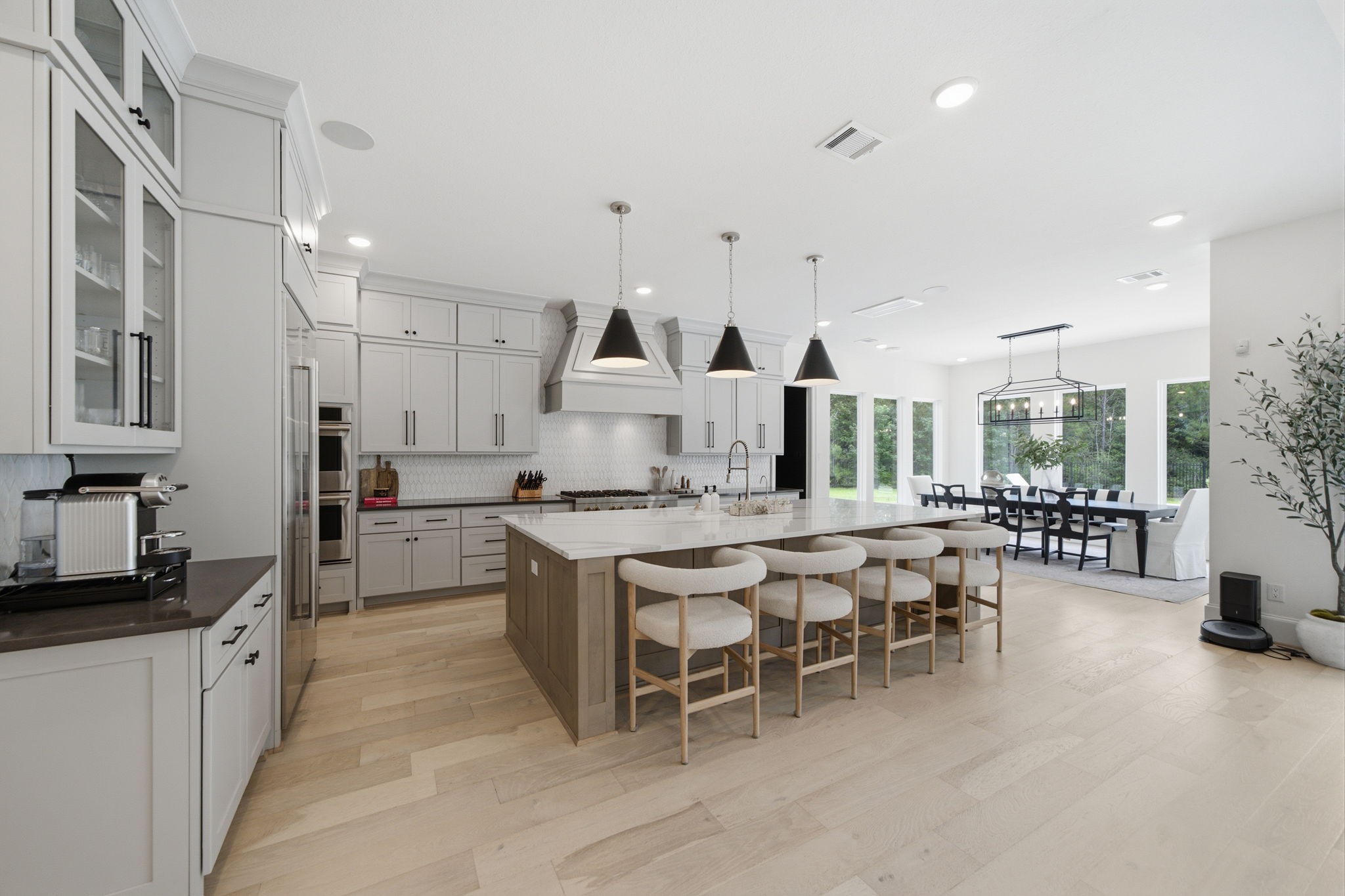 Spacious and elegant kitchen with modern cabinetry, a large island with seating, and stylish pendant lighting, seamlessly flowing into a bright dining area with large windows. Spacious and elegant kitchen with modern cabinetry, a large island with seating, and stylish pendant lighting, seamlessly flowing into a bright dining area with large windows.