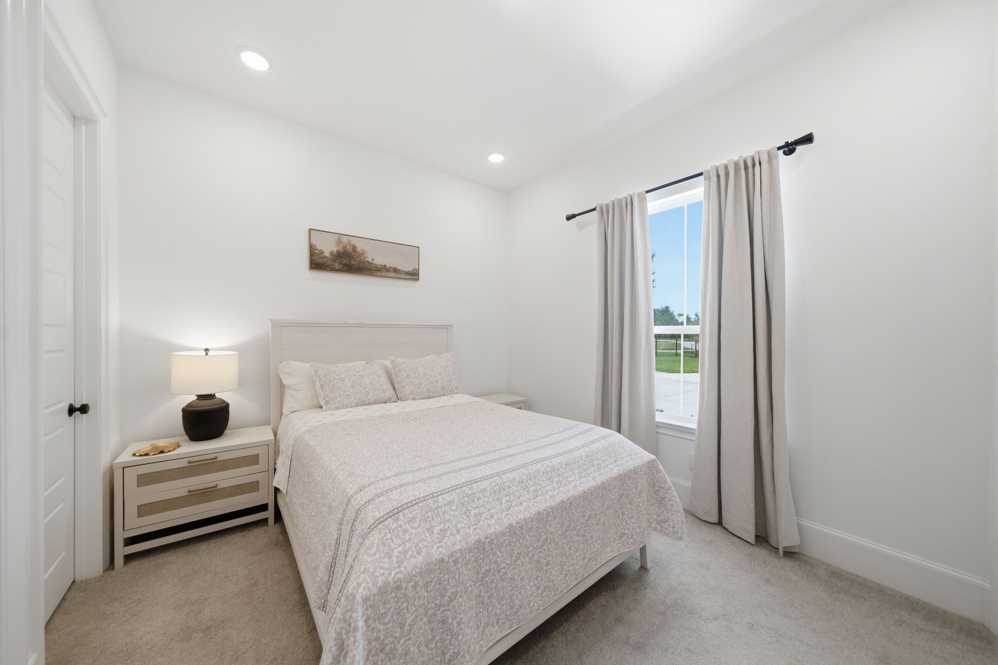 Bright and inviting bedroom featuring a cozy bed, soft carpeting, and a large window with elegant drapes, offering plenty of natural light.