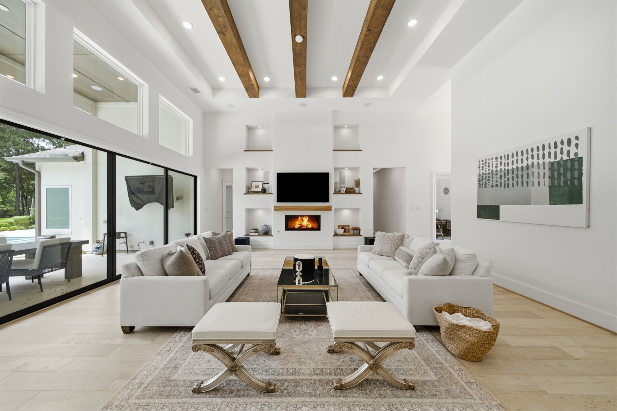 Stunning living room with high ceilings, exposed wooden beams, and abundant natural light from floor-to-ceiling windows. Features a modern fireplace, sleek built-in shelving, and an open view to the patio and pool area, perfect for entertaining. Stunning living room with high ceilings, exposed wooden beams, and abundant natural light from floor-to-ceiling windows. Features a modern fireplace, sleek built-in shelving, and an open view to the patio and pool area, perfect for entertaining.