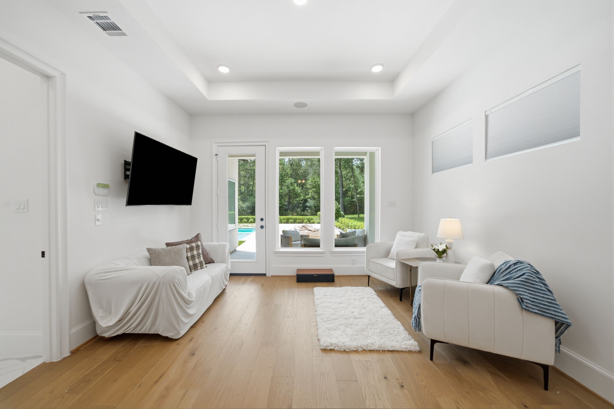 Bright and inviting living area with sleek hardwood floors, modern furnishings, and large windows offering scenic views of the backyard and pool. Bright and inviting living area with sleek hardwood floors, modern furnishings, and large windows offering scenic views of the backyard and pool.