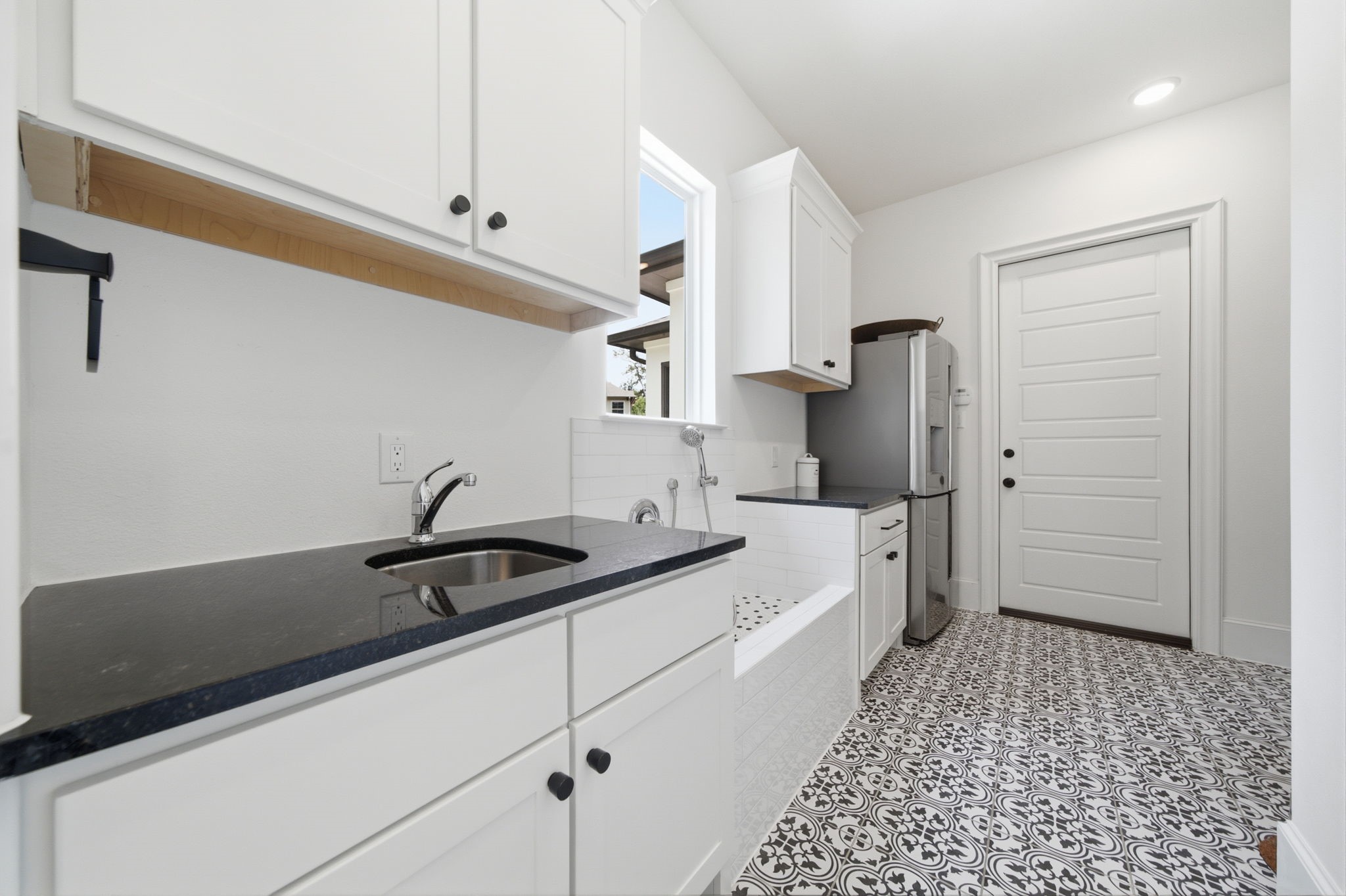 Stylish laundry room featuring elegant black countertops, crisp white cabinetry, and eye-catching patterned floor tiles, offering both functionality and charm.