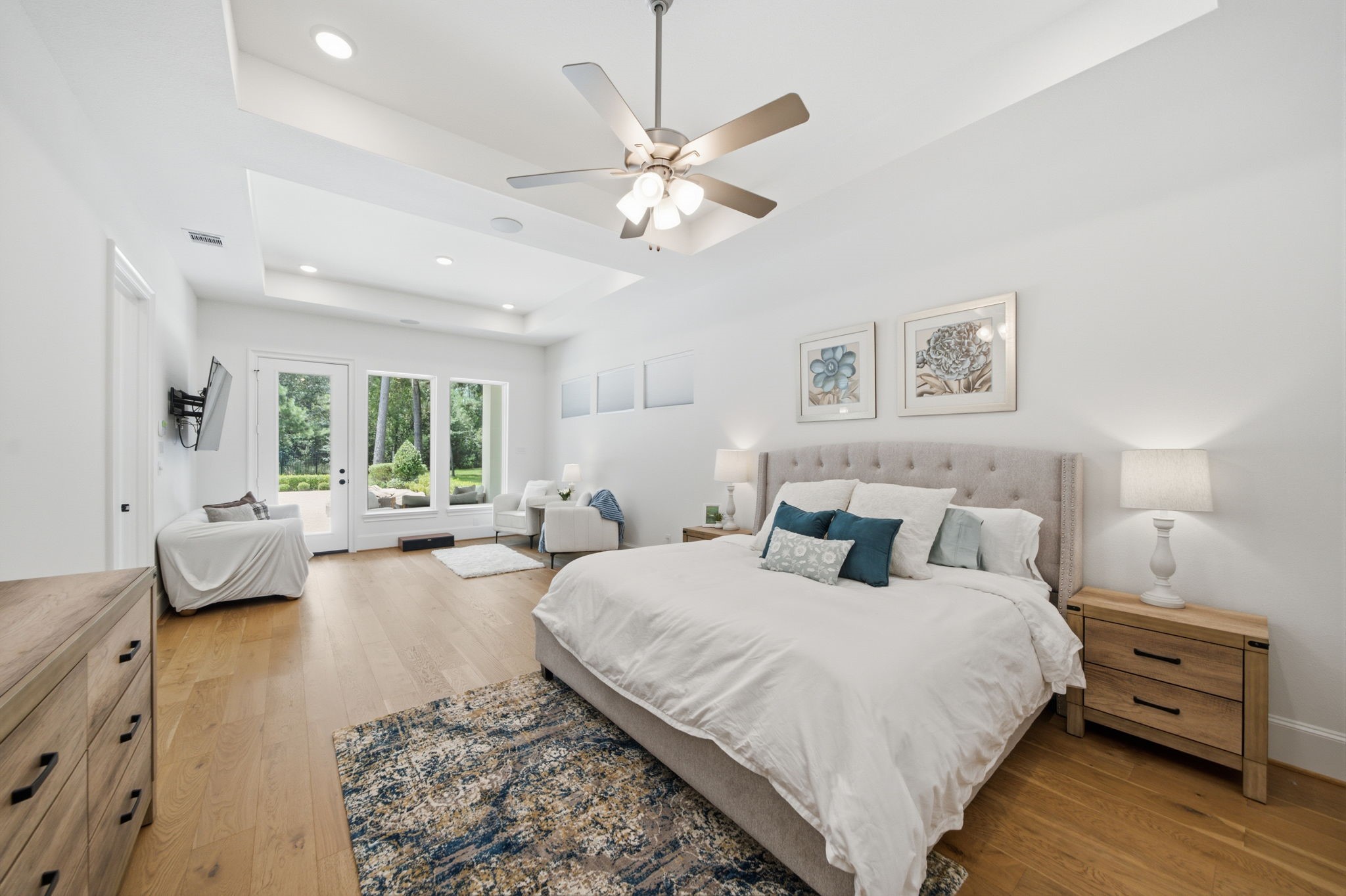 Spacious and bright bedroom with elegant tray ceiling, hardwood floors, and large windows offering serene views.