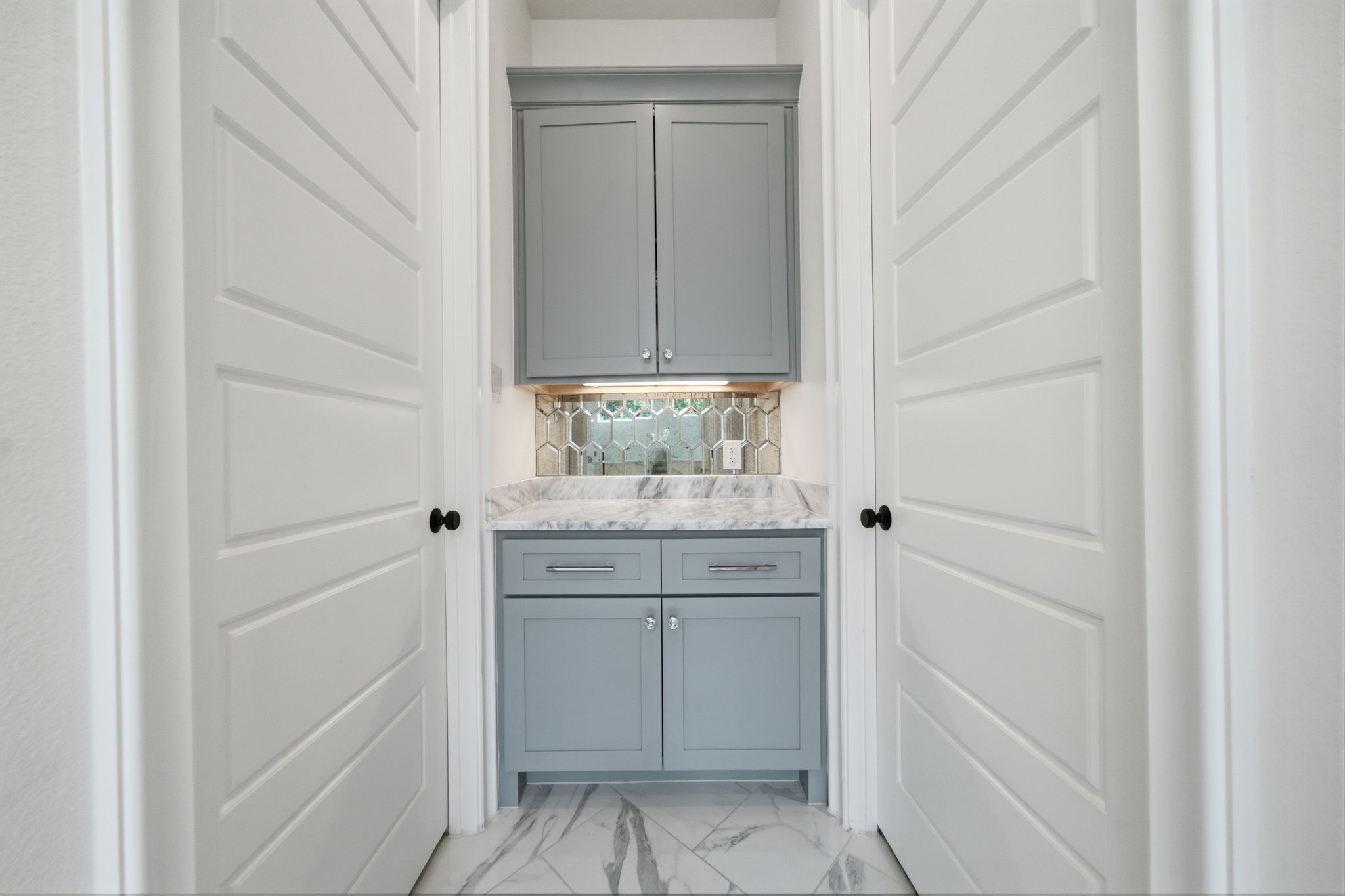Elegant hallway nook featuring sleek gray cabinetry with marble countertops and a stylish hexagonal tile backsplash.