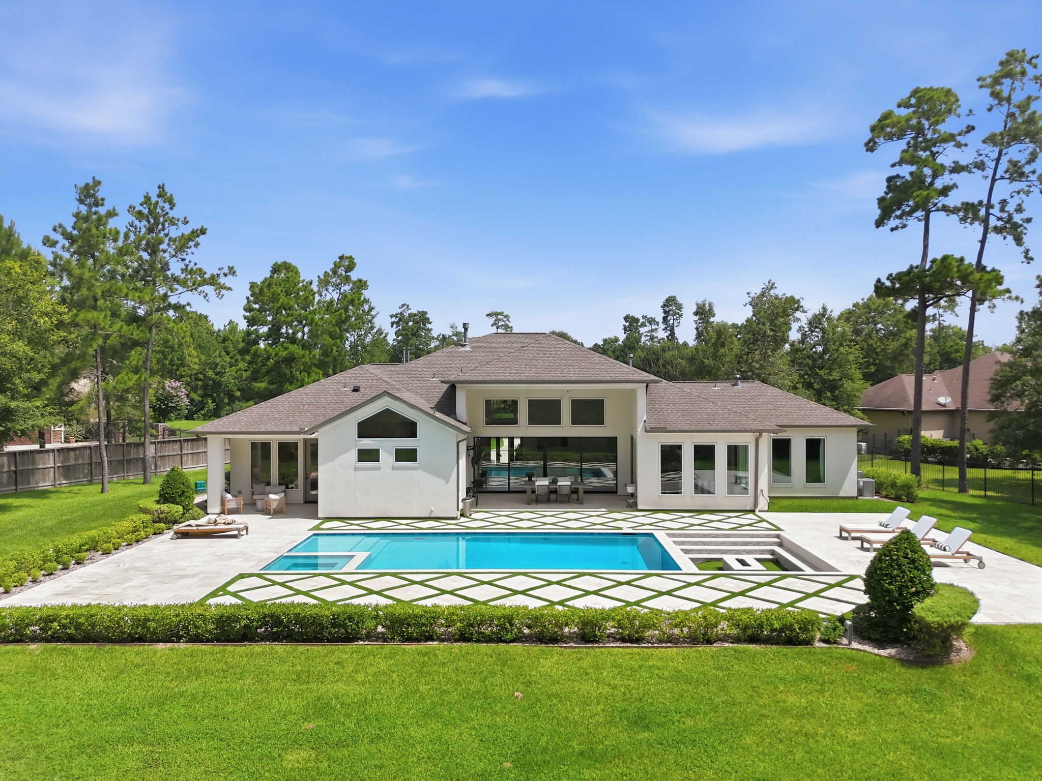 Luxurious modern home with expansive backyard featuring a pristine pool, surrounded by lush greenery and spacious patio areas, perfect for entertaining and relaxation.