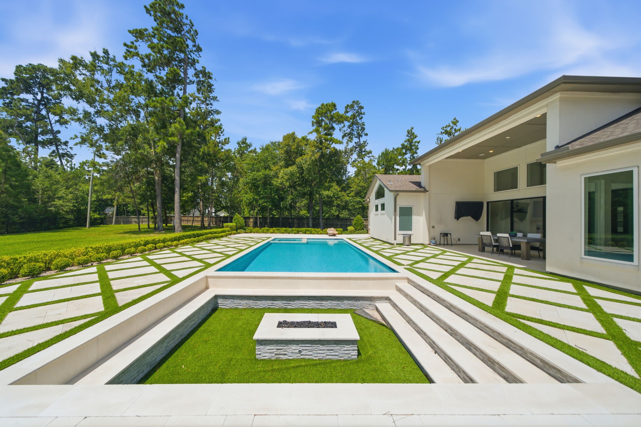 Luxurious backyard oasis featuring a sleek swimming pool, modern patio with a covered dining area, and elegant landscaping surrounded by lush greenery.