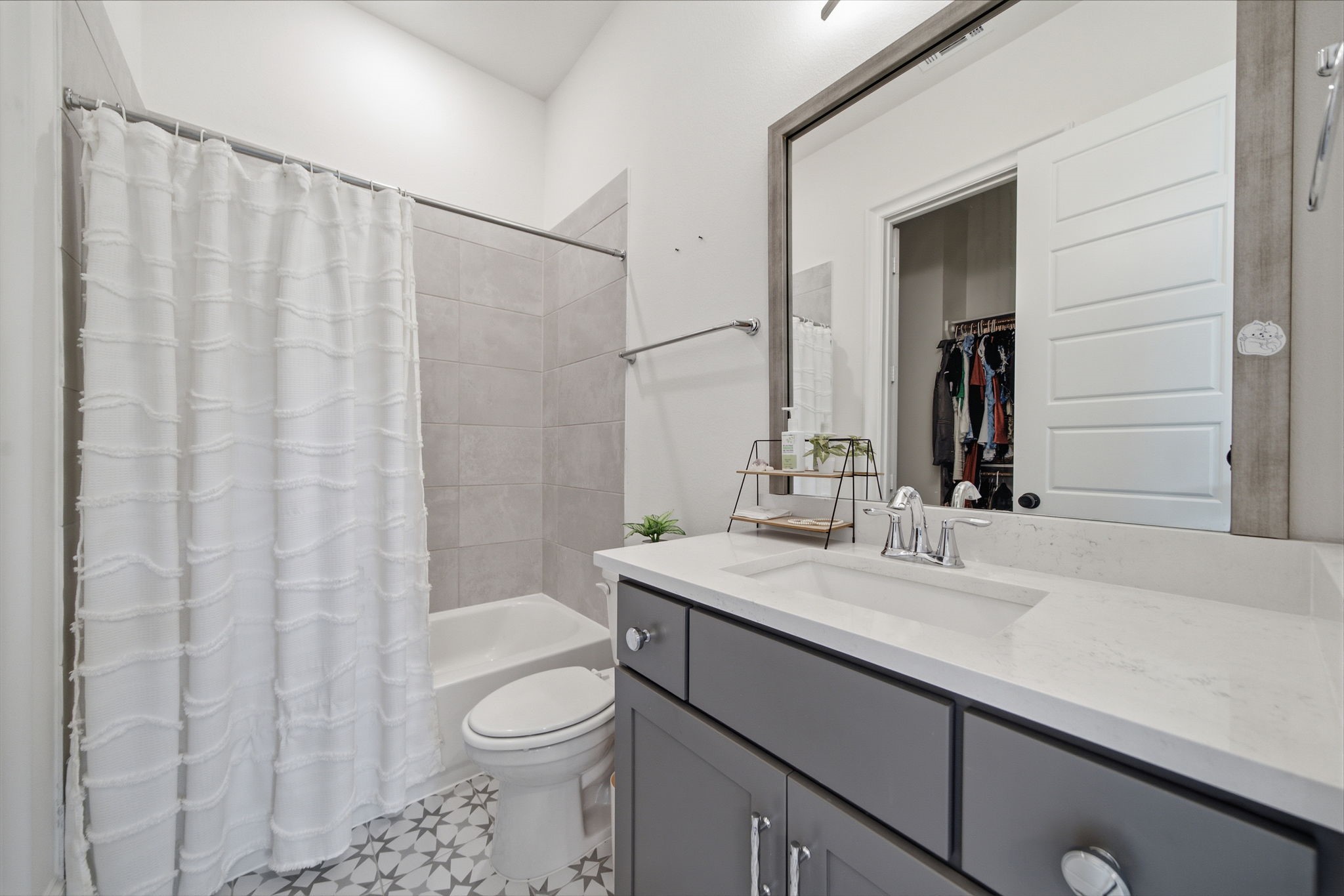 Modern bathroom featuring sleek gray cabinetry, a spacious mirror, and a stylish vanity with a polished countertop. The shower-tub combo is complemented by elegant tile work and a bright curtain, creating a fresh and inviting space.