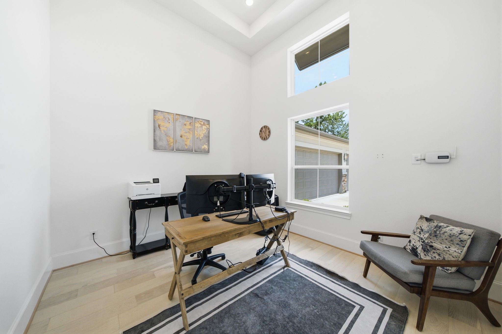 Bright and airy home office with high ceilings, a large window, and stylish wood flooring, perfect for productivity.