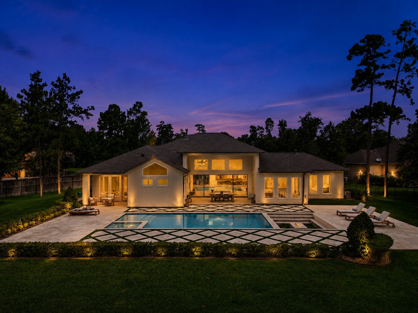 Experience luxury living in this stunning home featuring a beautifully lit backyard with a modern pool, spacious patio, gas fire pit, and elegant landscaping, all set against a picturesque evening sky.