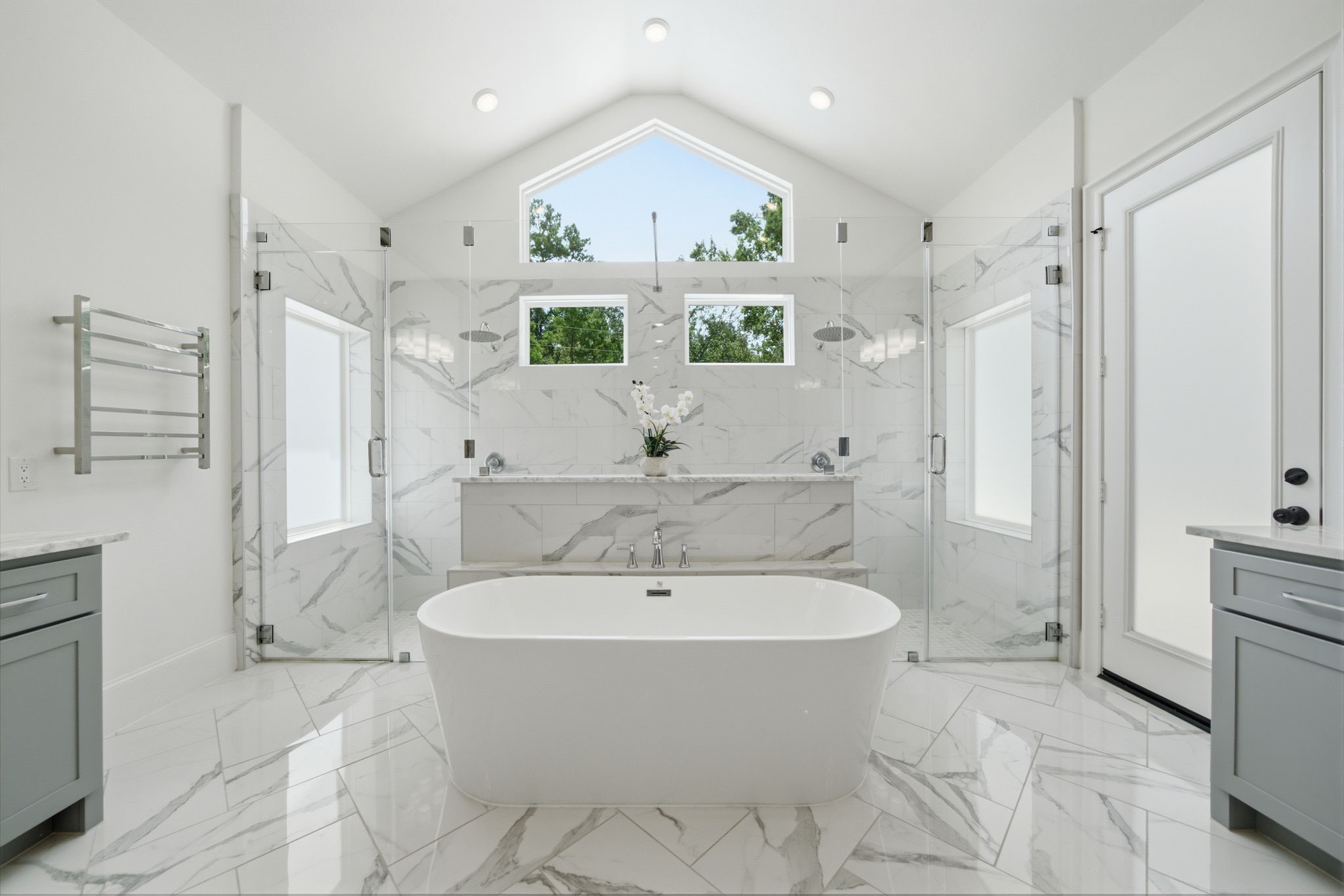 Luxurious bathroom featuring a freestanding tub, dual glass-enclosed showers, and elegant marble finishes, all under a vaulted ceiling with abundant natural light.