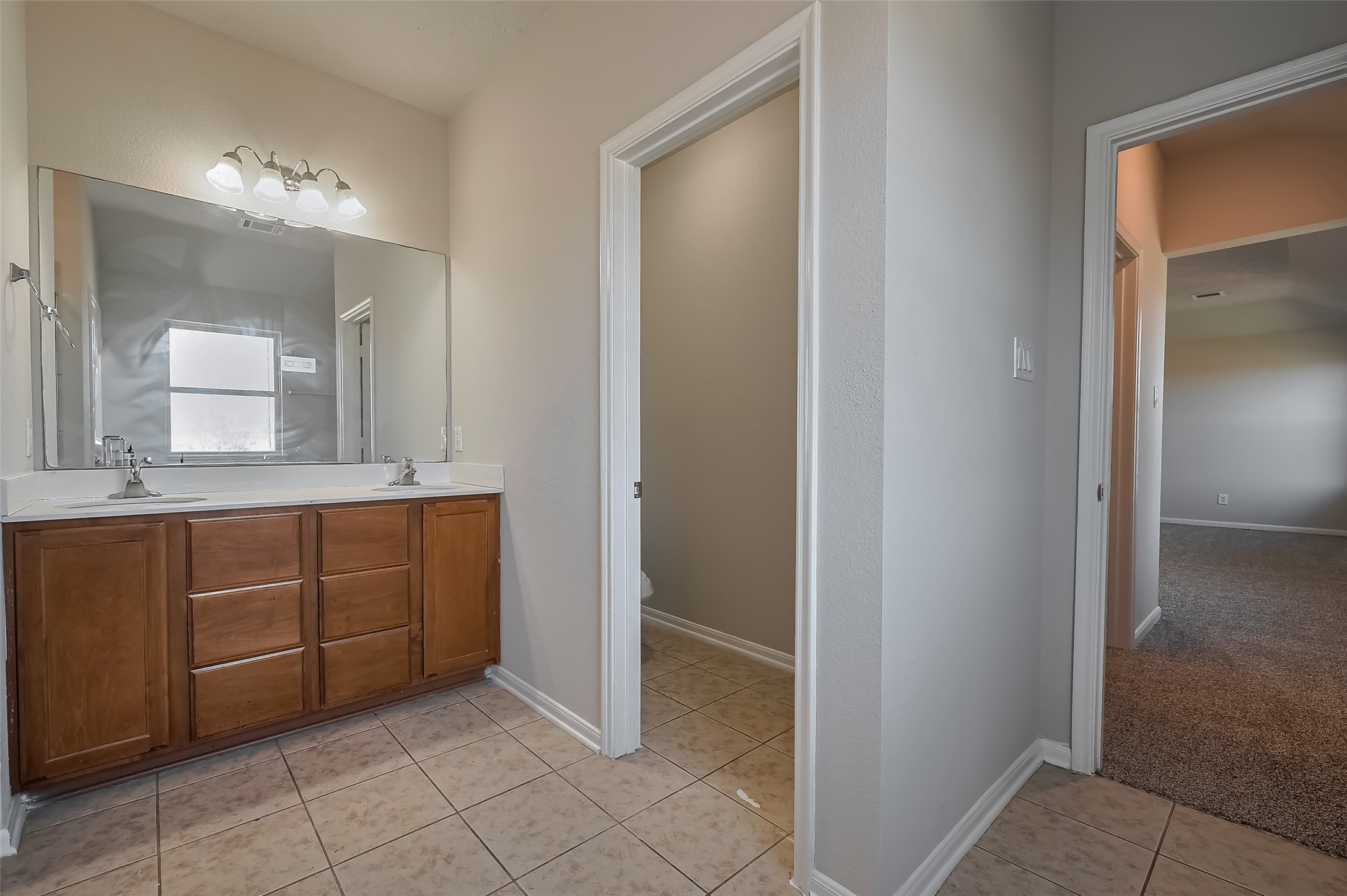 Primary Bathroom with dual sinks, a large mirror & wooden cabinetry.