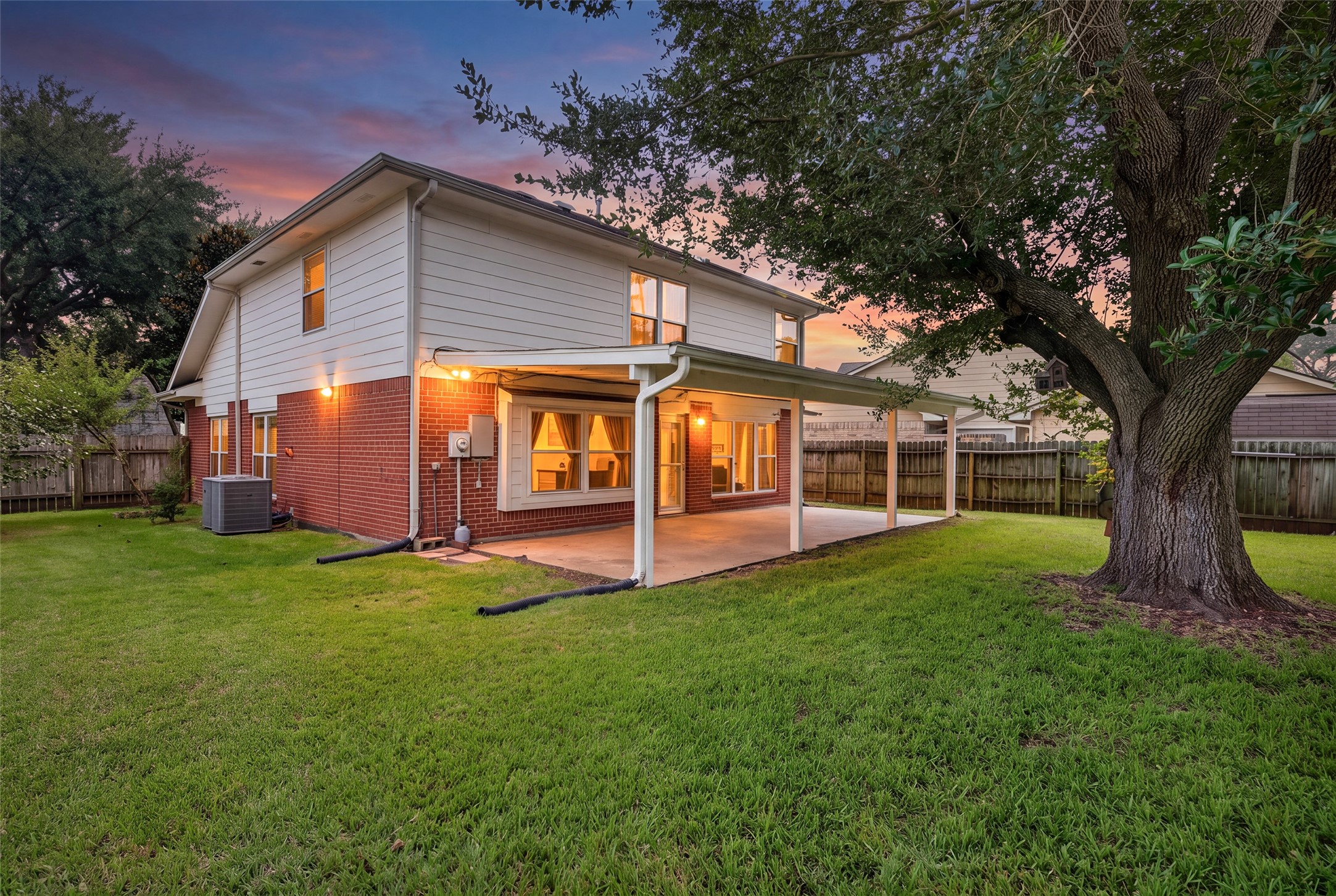 As twilight sets, the peaceful backyard comes to life with glowing indoor lights visible through the expansive windows and glass doors.