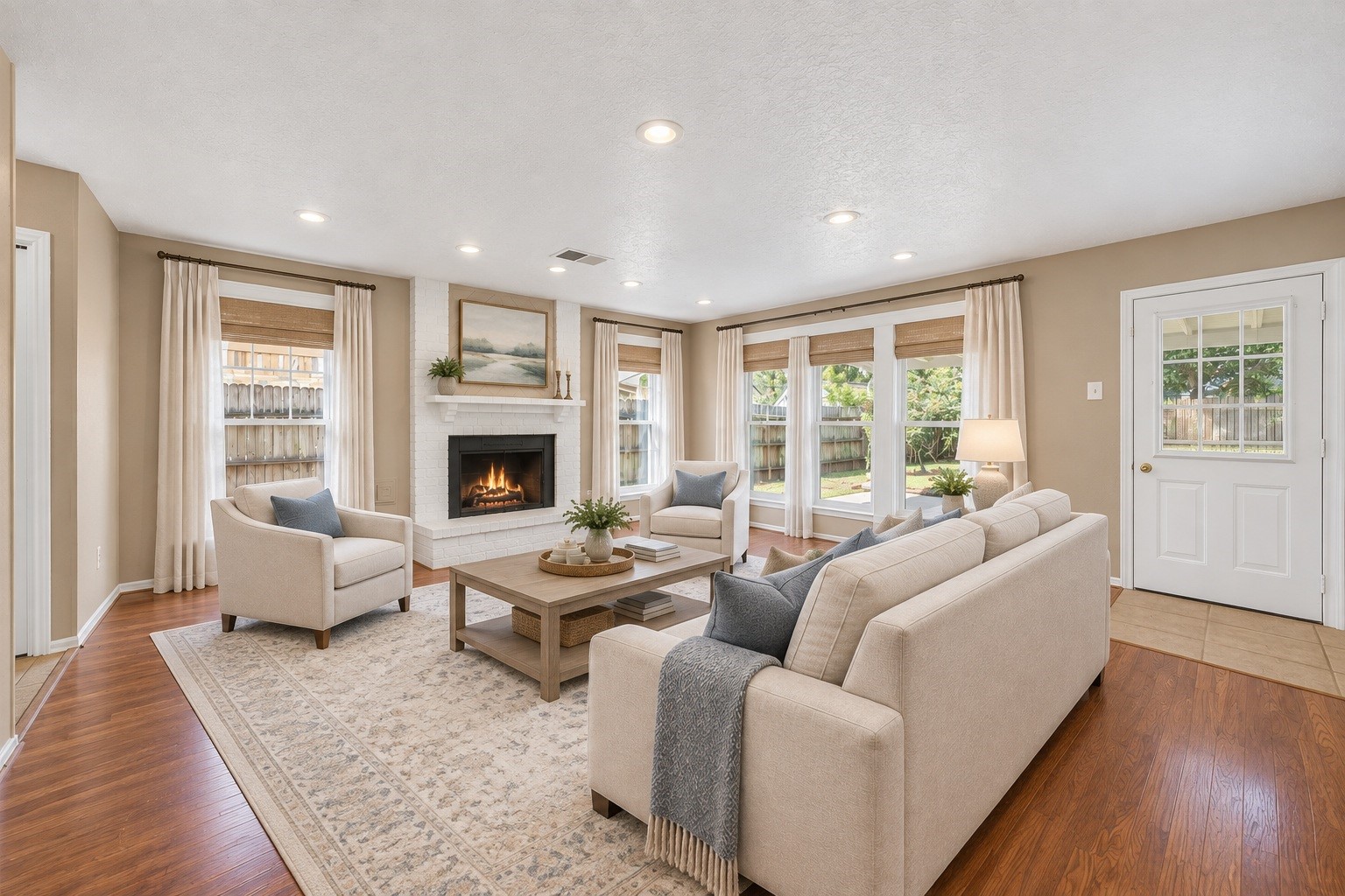 Step right into a cozy, light-filled living room framed by large windows that offer scenic views of the lush backyard and patio area.