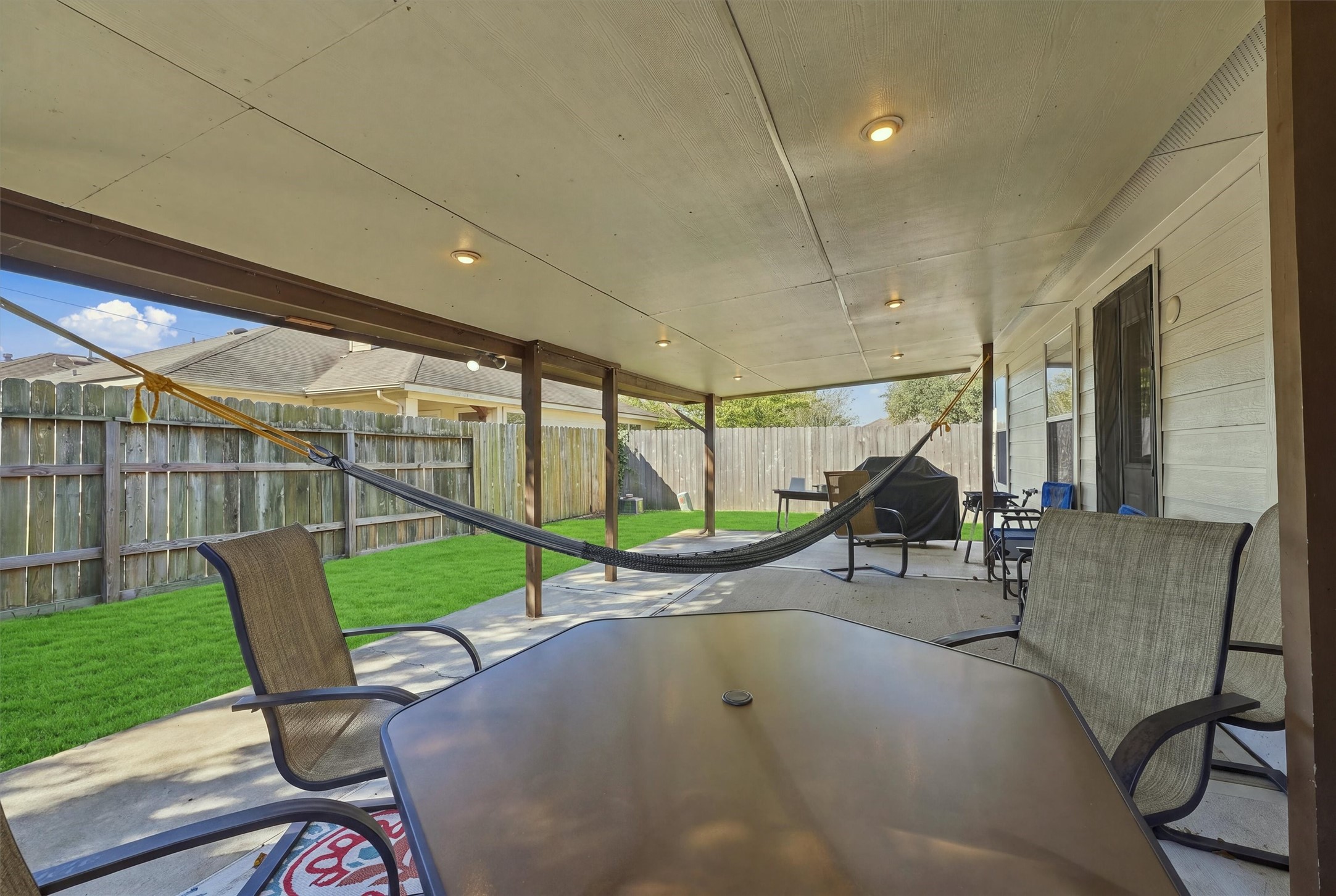 Spacious covered patio featuring comfortable seating and a hammock, perfect for relaxing and entertaining in a private fenced backyard.