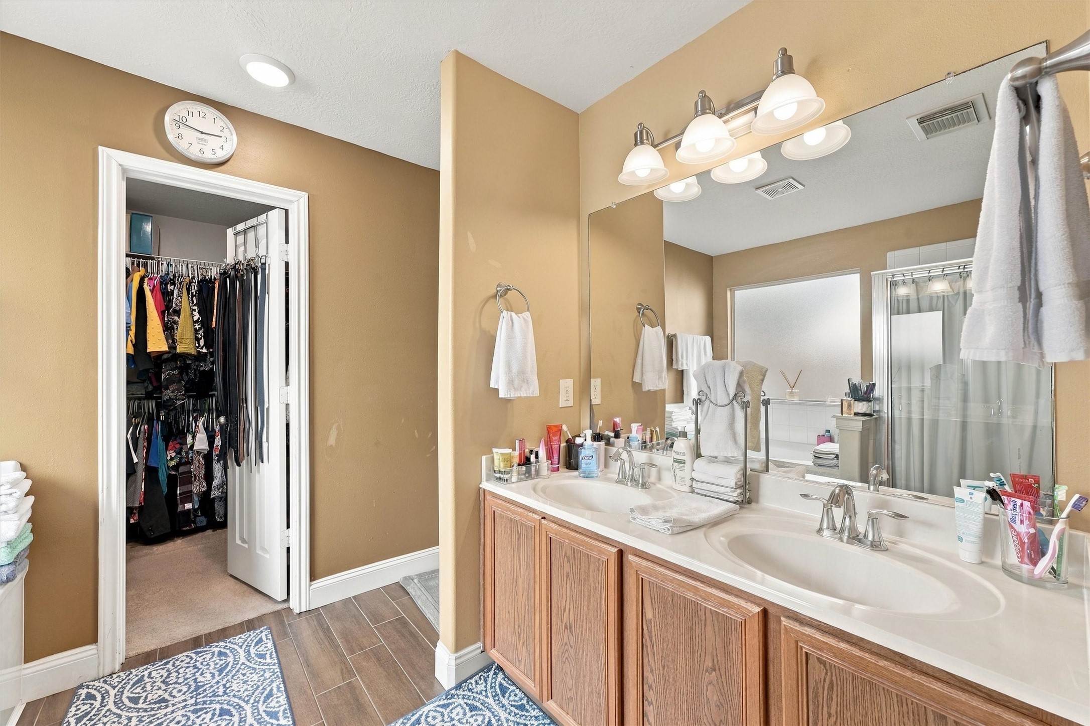 Elegant bathroom featuring a double vanity with ample counter space, warm lighting, and a large mirror. Attached is a spacious walk-in closet, offering plenty of storage.