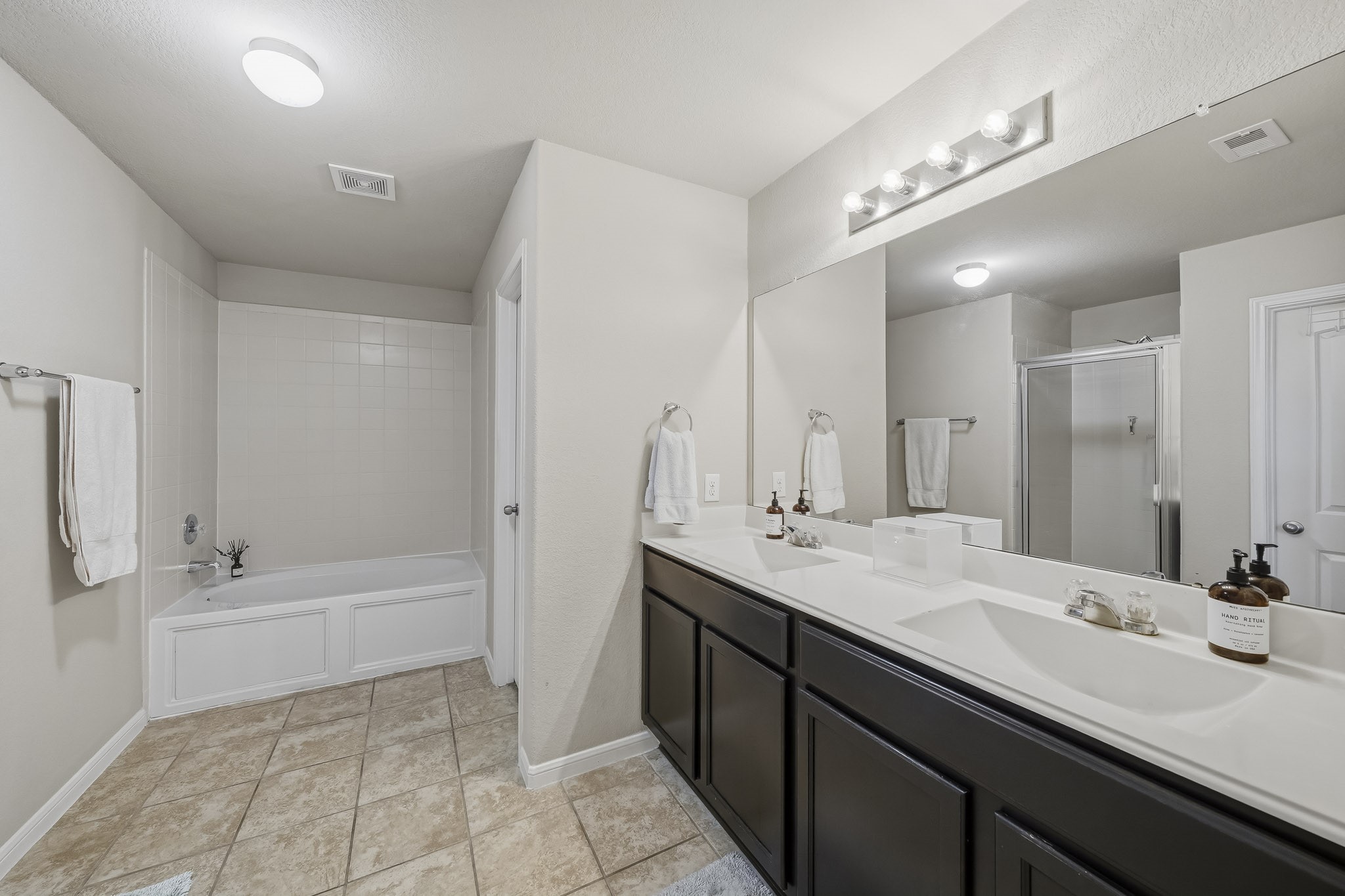 The spacious primary bathroom with walk-in closet, features dual vanities, a soaking tub, a separate glass-enclosed shower, and generous counter space for a comfortable daily routine.