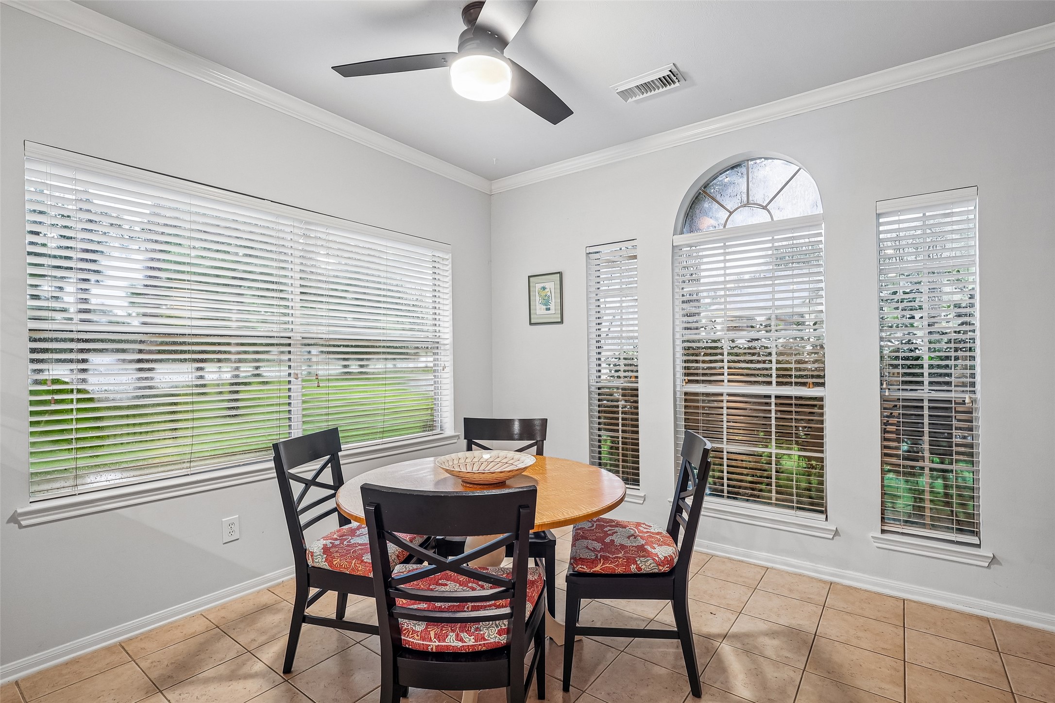 Bright dining area with large windows, tile flooring, and a ceiling fan, offering a cozy setting for meals.