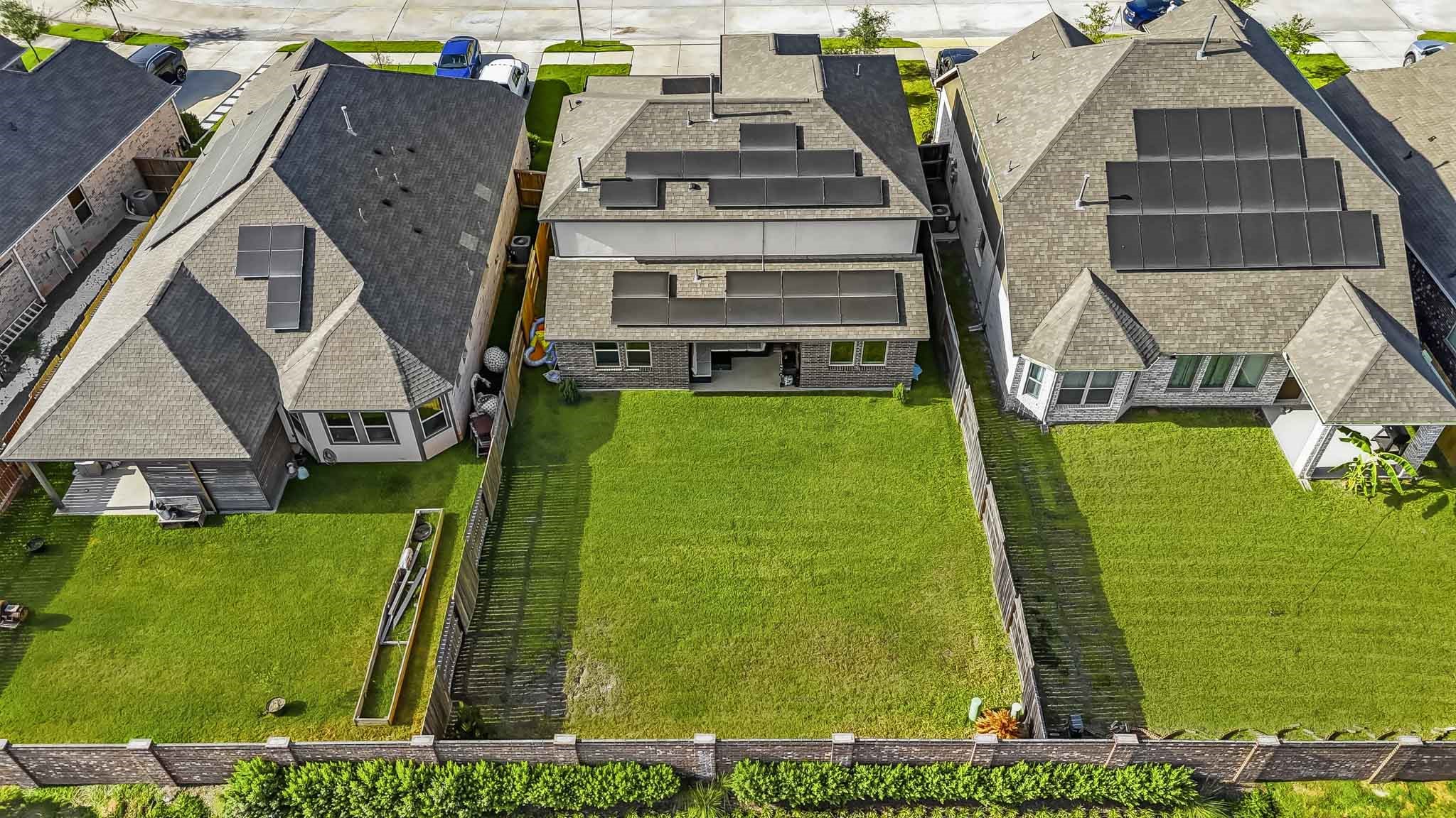 This aerial view showcases the homes spacious backyard and 6,351 sq. ft. lot, offering a generous stretch of fully fenced green space. The expansive lawn provides plenty of room for outdoor entertaining, recreation, a play area, or future landscaping possibilities, while the covered patio extends the homes living space outdoors. Solar panels can also be seen across the roof, adding an energy-efficient feature.