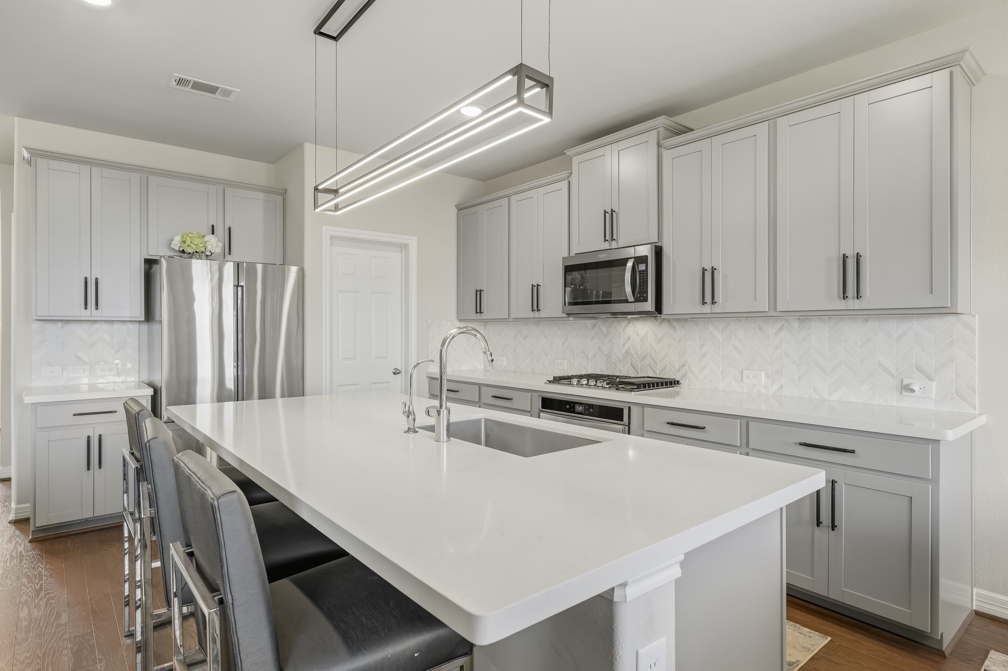 This beautifully updated kitchen features abundant cabinetry, sleek countertops, and a stylish herringbone tile backsplash. A large center island provides generous prep space, a built-in sink, and bar seating, making it ideal for everyday living and entertaining. Stainless steel appliances, a gas cooktop, modern fixtures, and contemporary lighting complete the bright, polished design.
