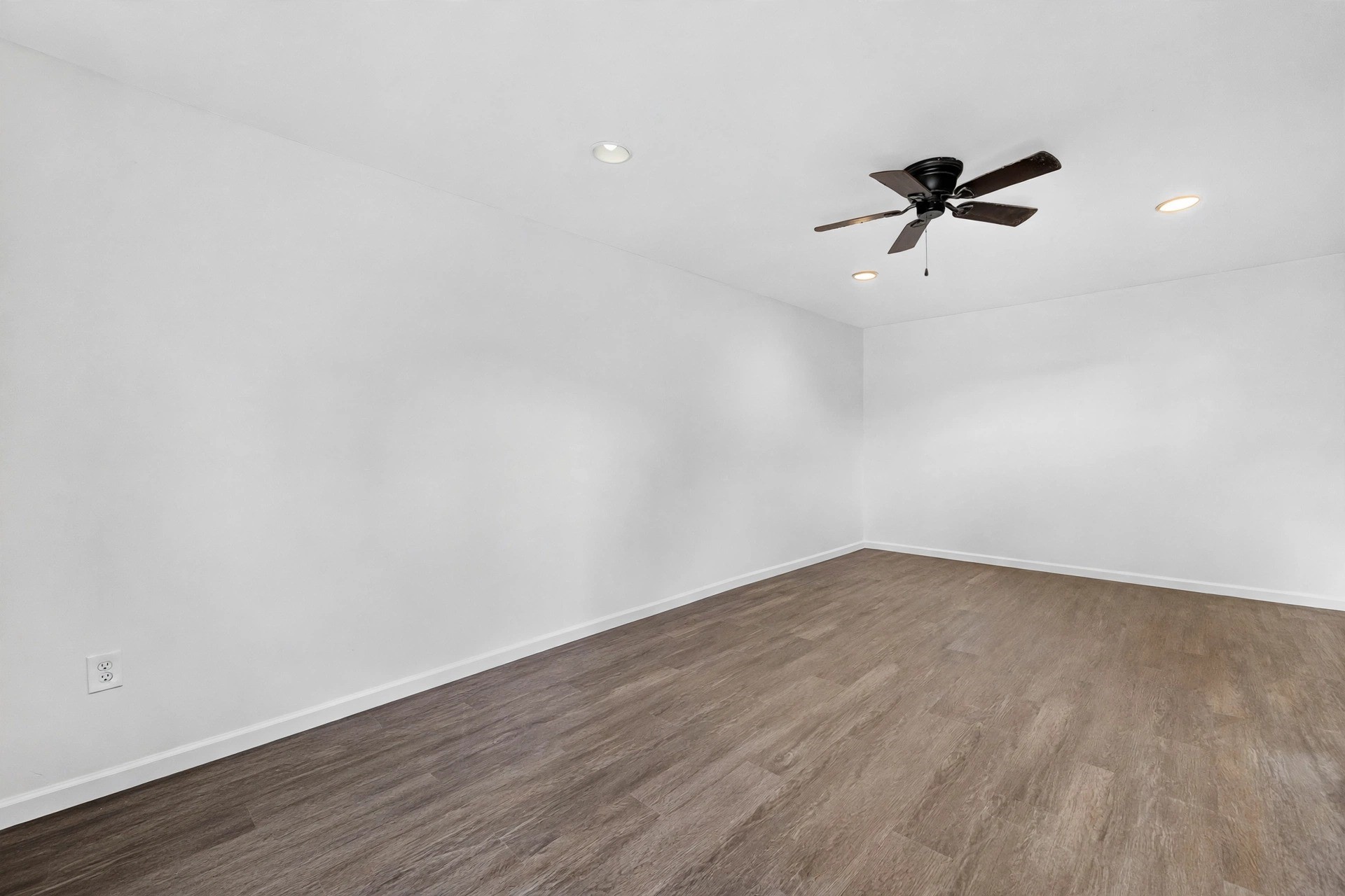 Flexible interior room with walls, wood-look flooring, a dark ceiling fan, and recessed lighting.