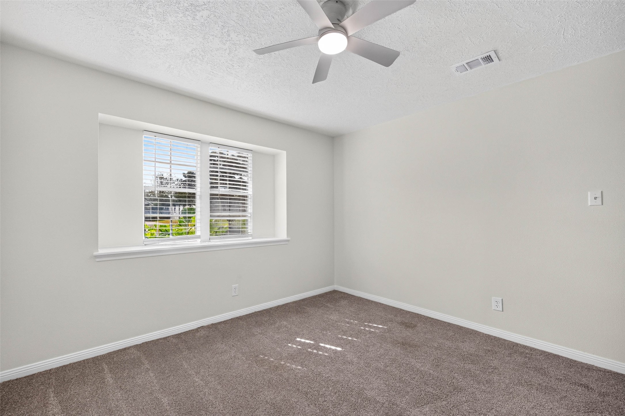 Another angle of the carpeted bedroom, with the same recessed double windows, ceiling fan, and soft neutral walls.