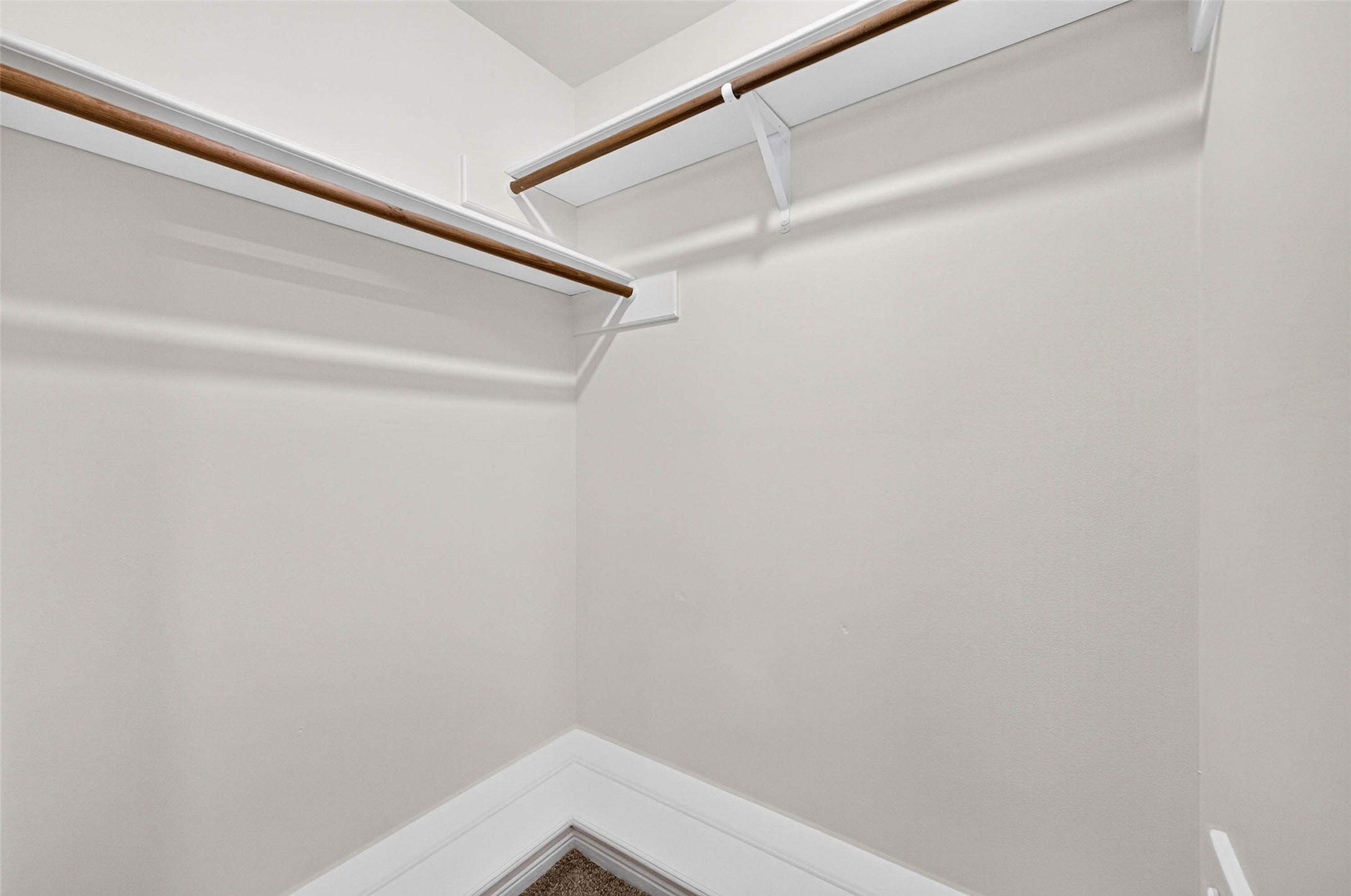 Walk-in closet with wood hanging rods and shelving running along two walls.