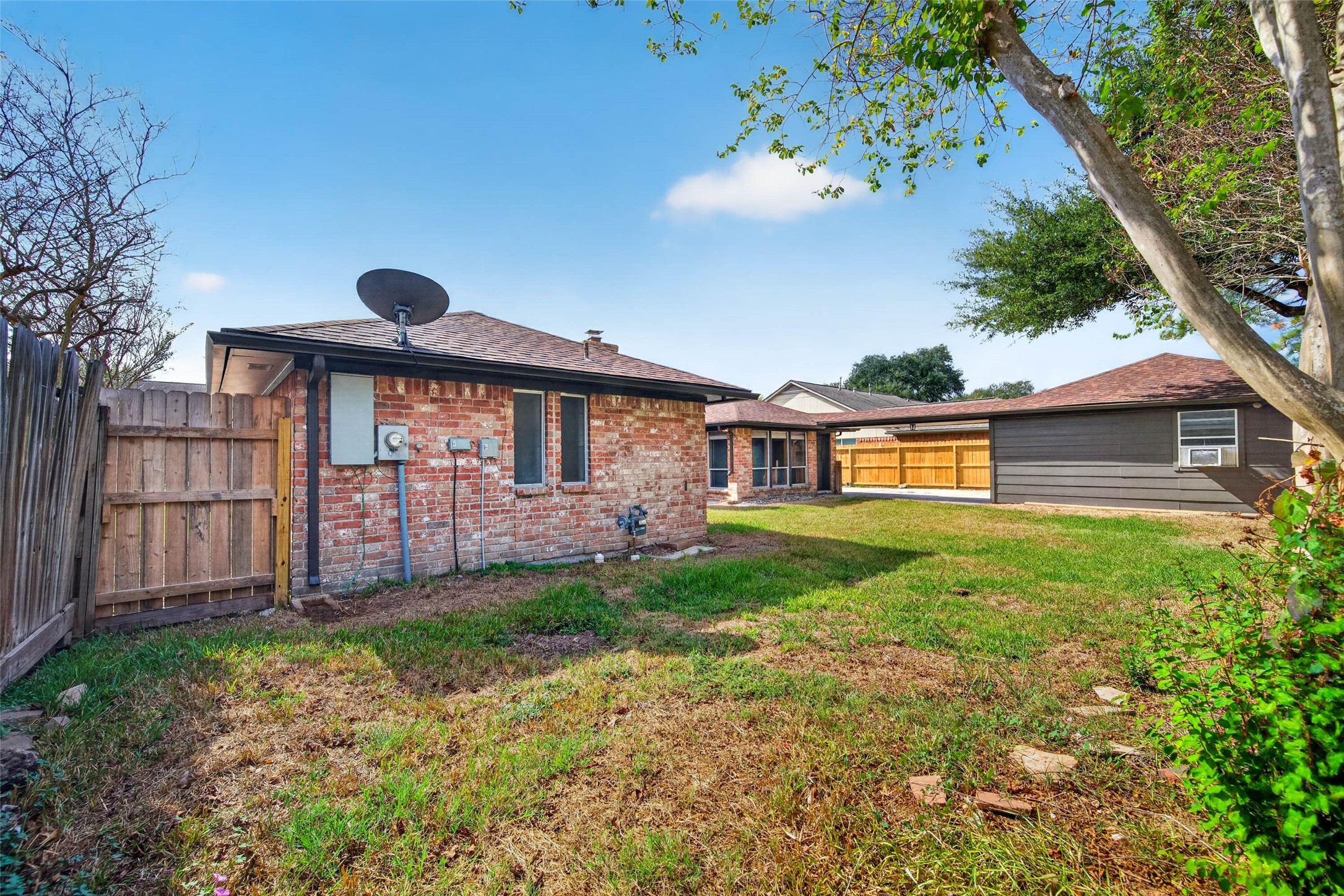 Side yard view with the brick side of the home, wooden fencing, and lawn.