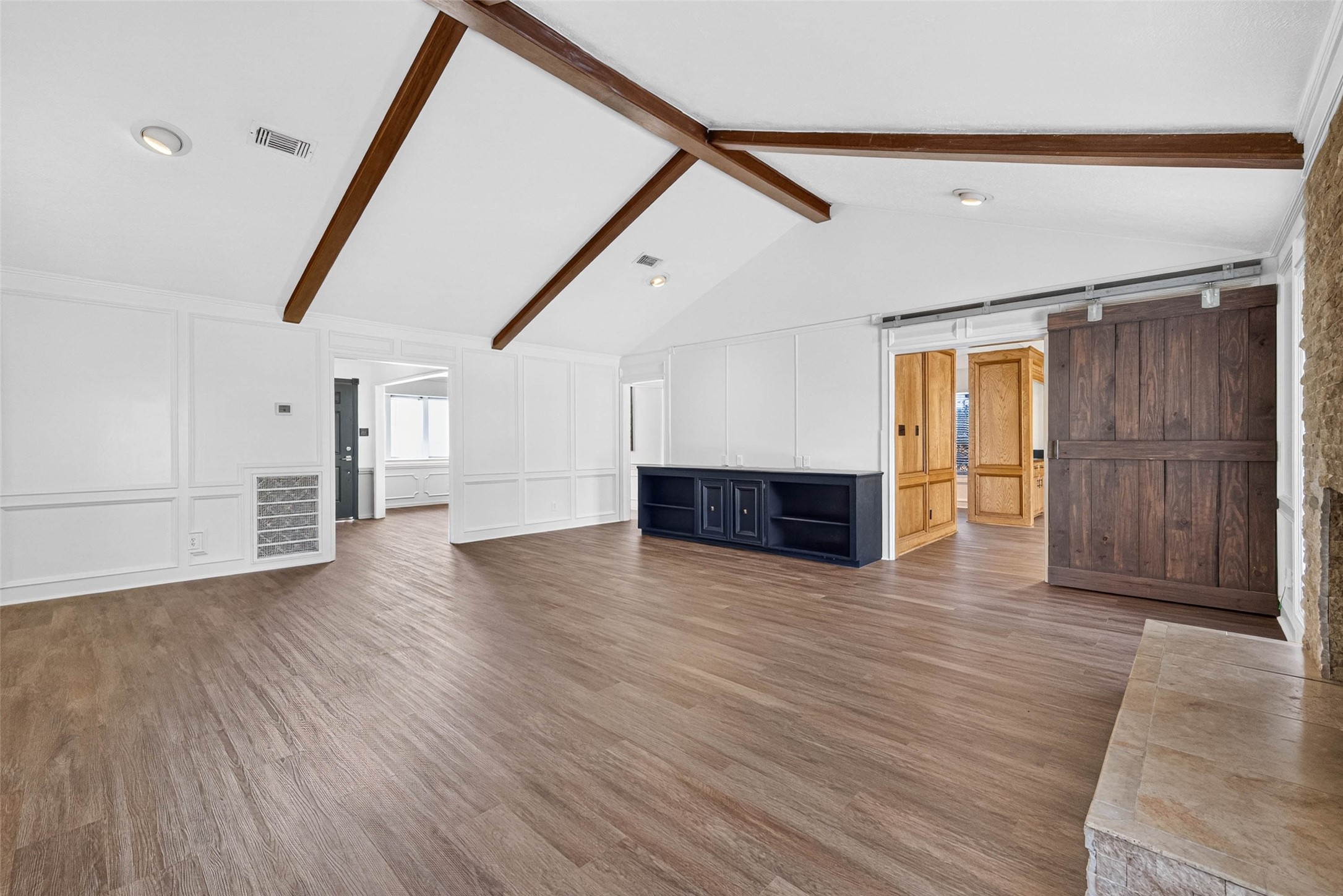 Living room angle centered on the dark wood sliding barn door, with crossing beams, paneled walls, and the stone fireplace hearth at the edge.