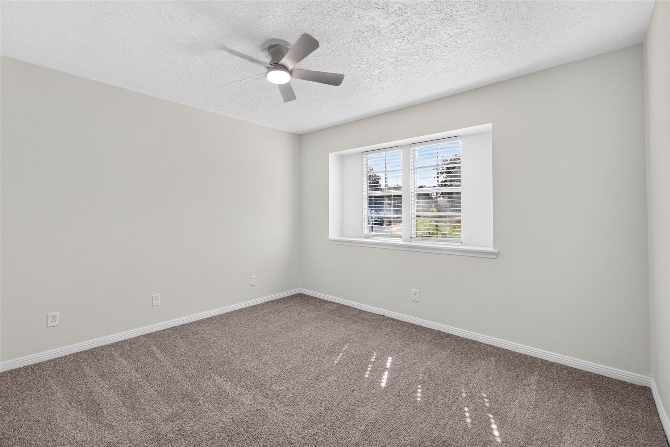 Carpeted bedroom with two windows set in a recessed niche, a ceiling fan with light, and sunlight falling across the carpet.