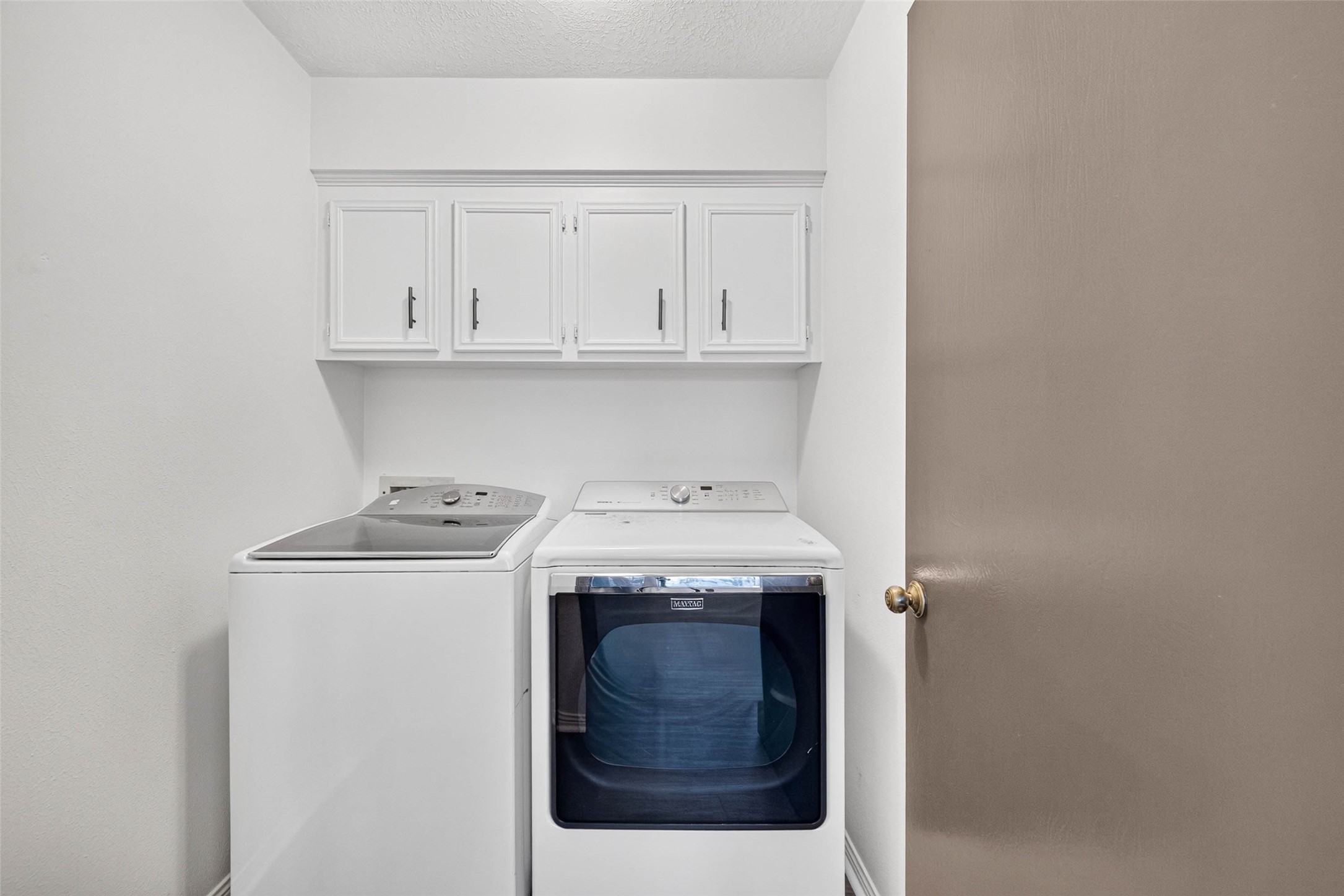 Laundry room with a washer and dryer side by side and upper cabinets for storage.