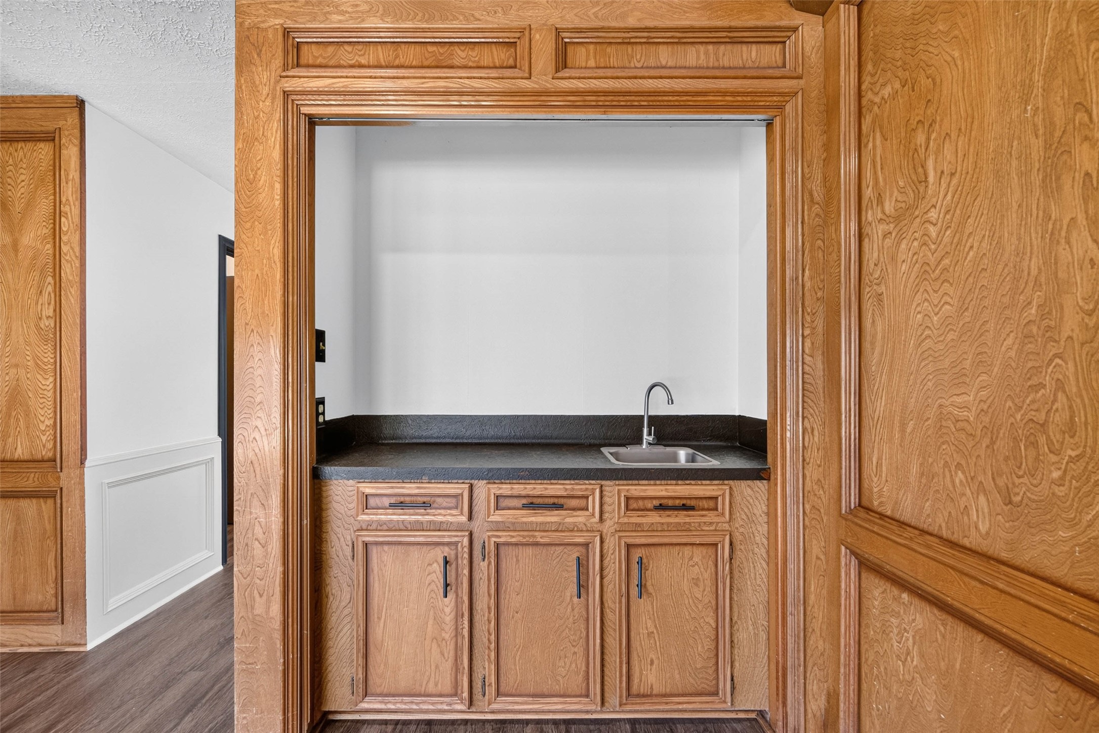 Close-up of the built-in bar nook, with wood cabinets, a dark countertop, and a sink framed by the room's wood paneling.