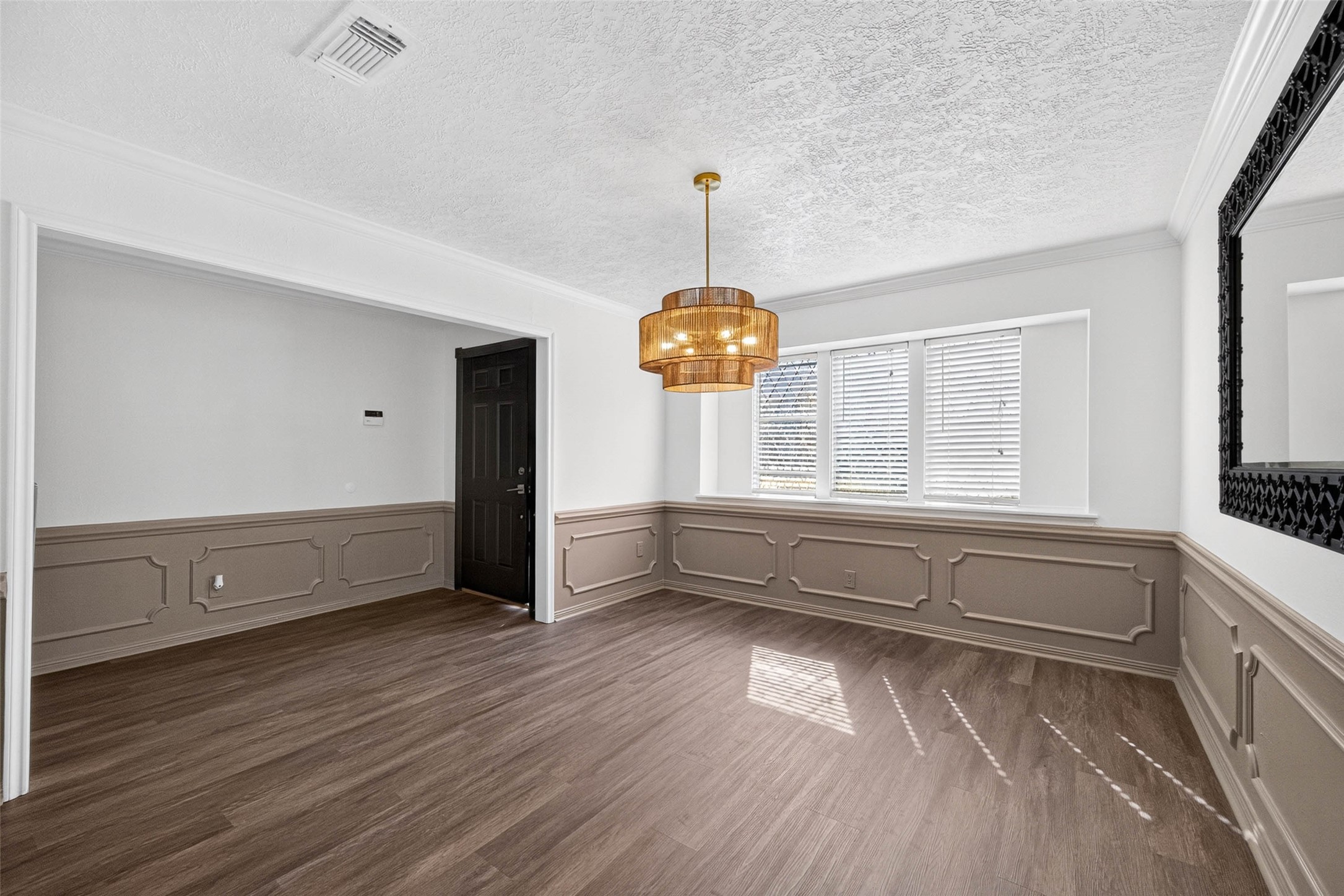 Front room with two-tone walls and raised-panel wainscoting, wood-look flooring, a tiered pendant light, and three windows with blinds.