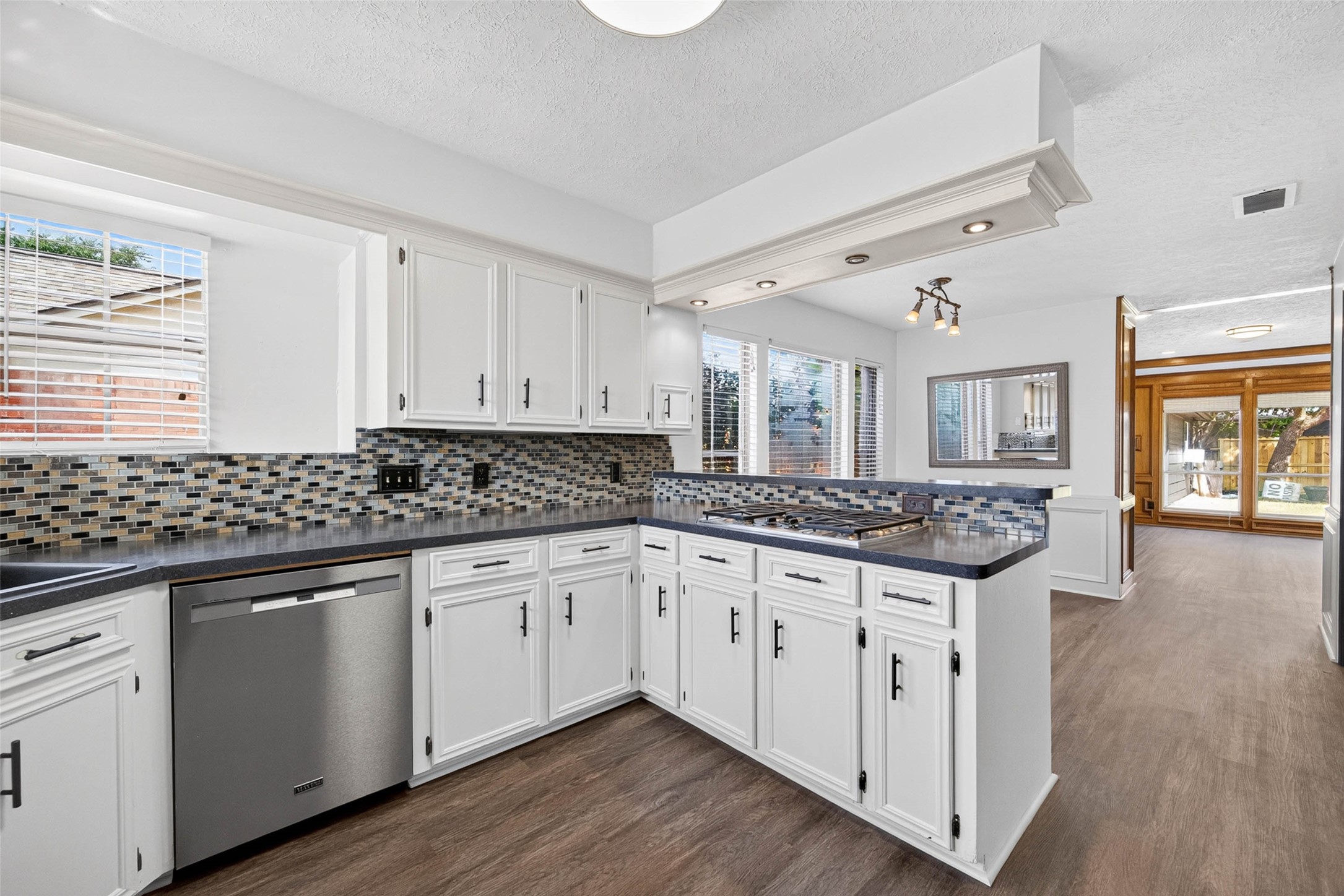 Wide kitchen view along the cabinetry and mosaic backsplash, with the gas cooktop on the peninsula and the dining area and paneled room opening beyond.